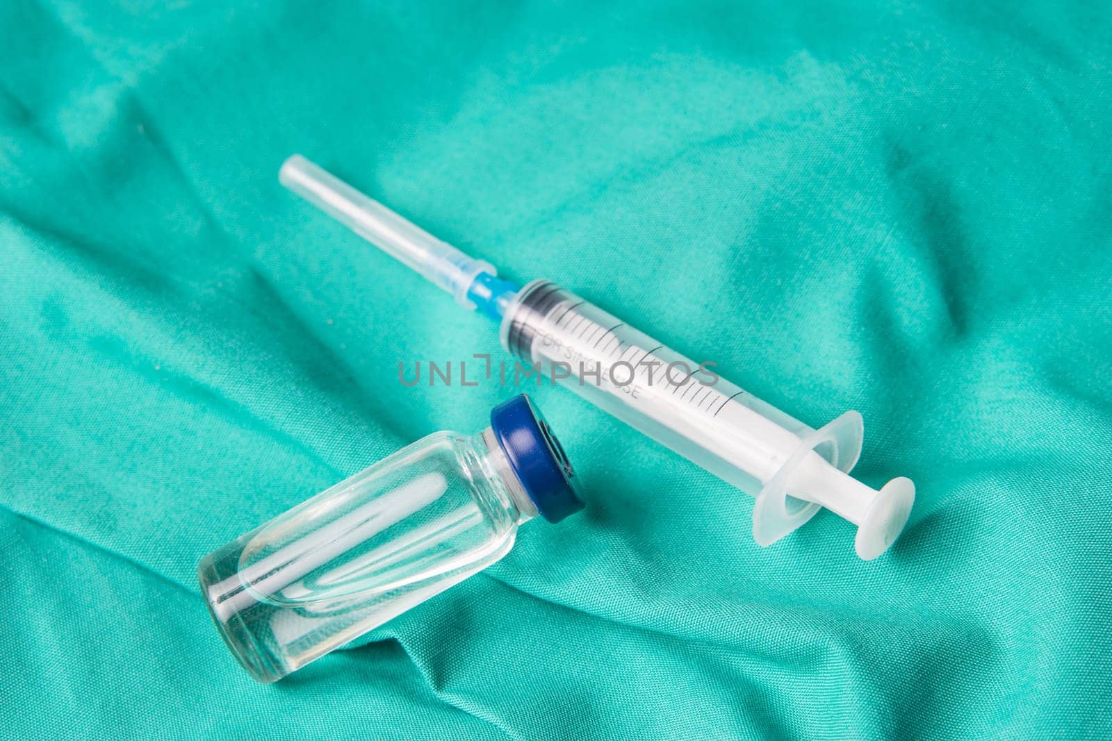 Medical syringe and vials lying on the hospital's green background. The background can be a textile part of a doctor or nurse's work uniform