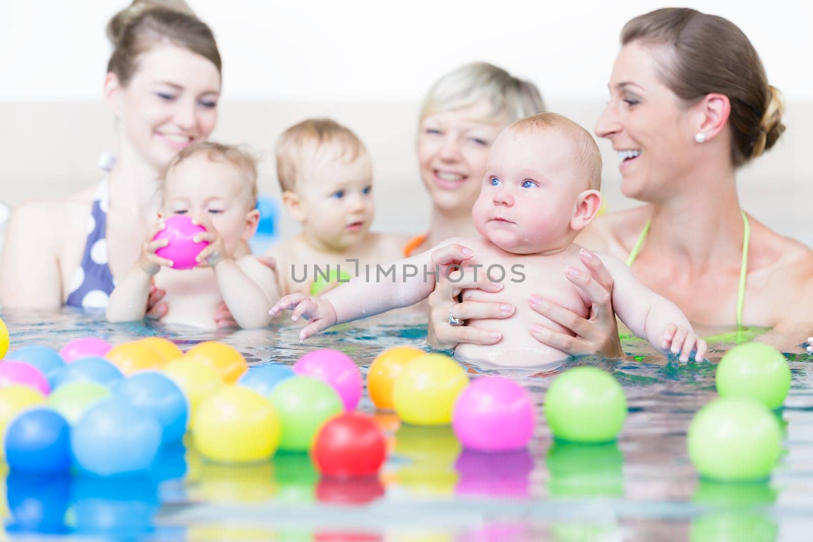 Moms and children at infant swimming lesson playing with balls