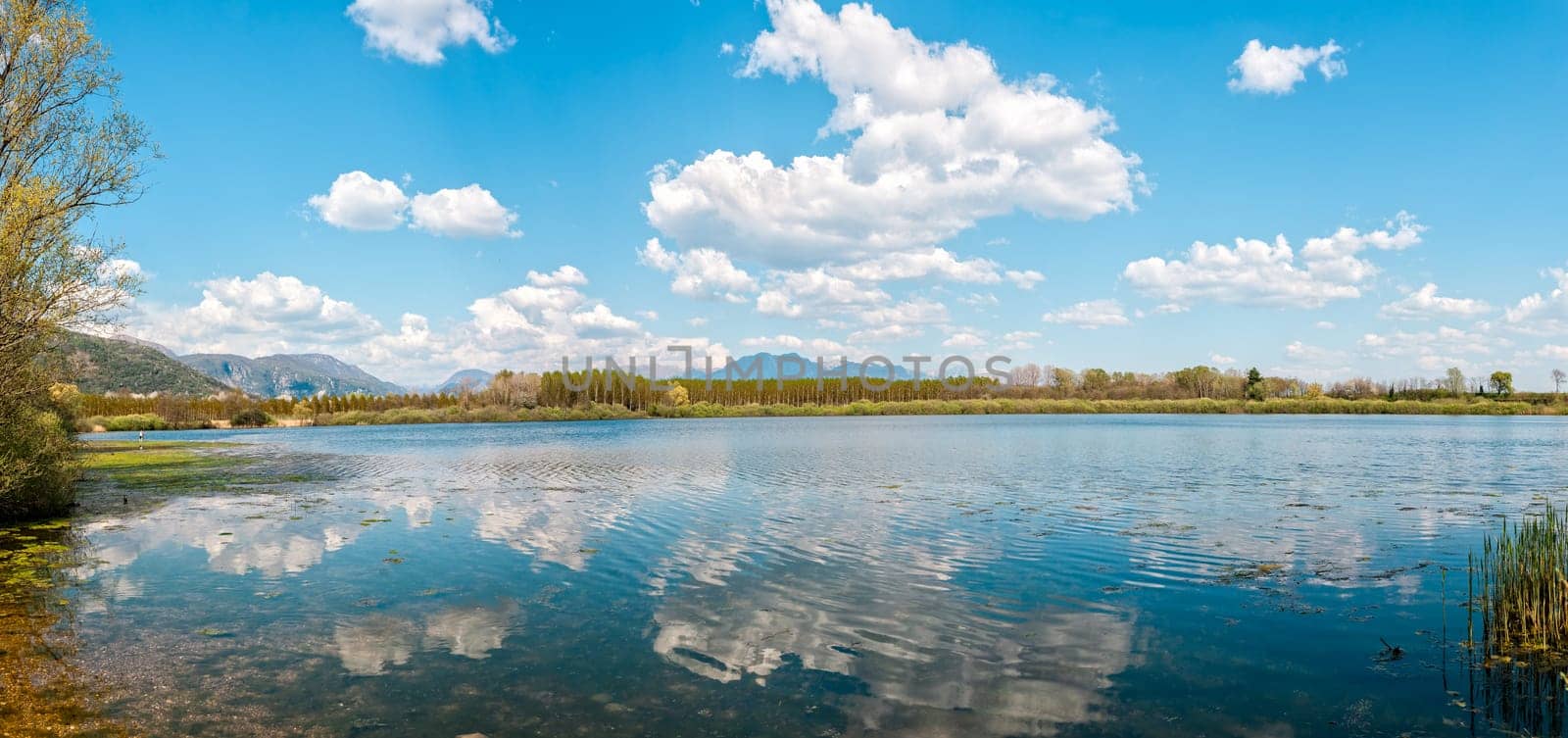 Landscape with lake,forest,blue sky and cloud.   Man fishing from the shore of lake .