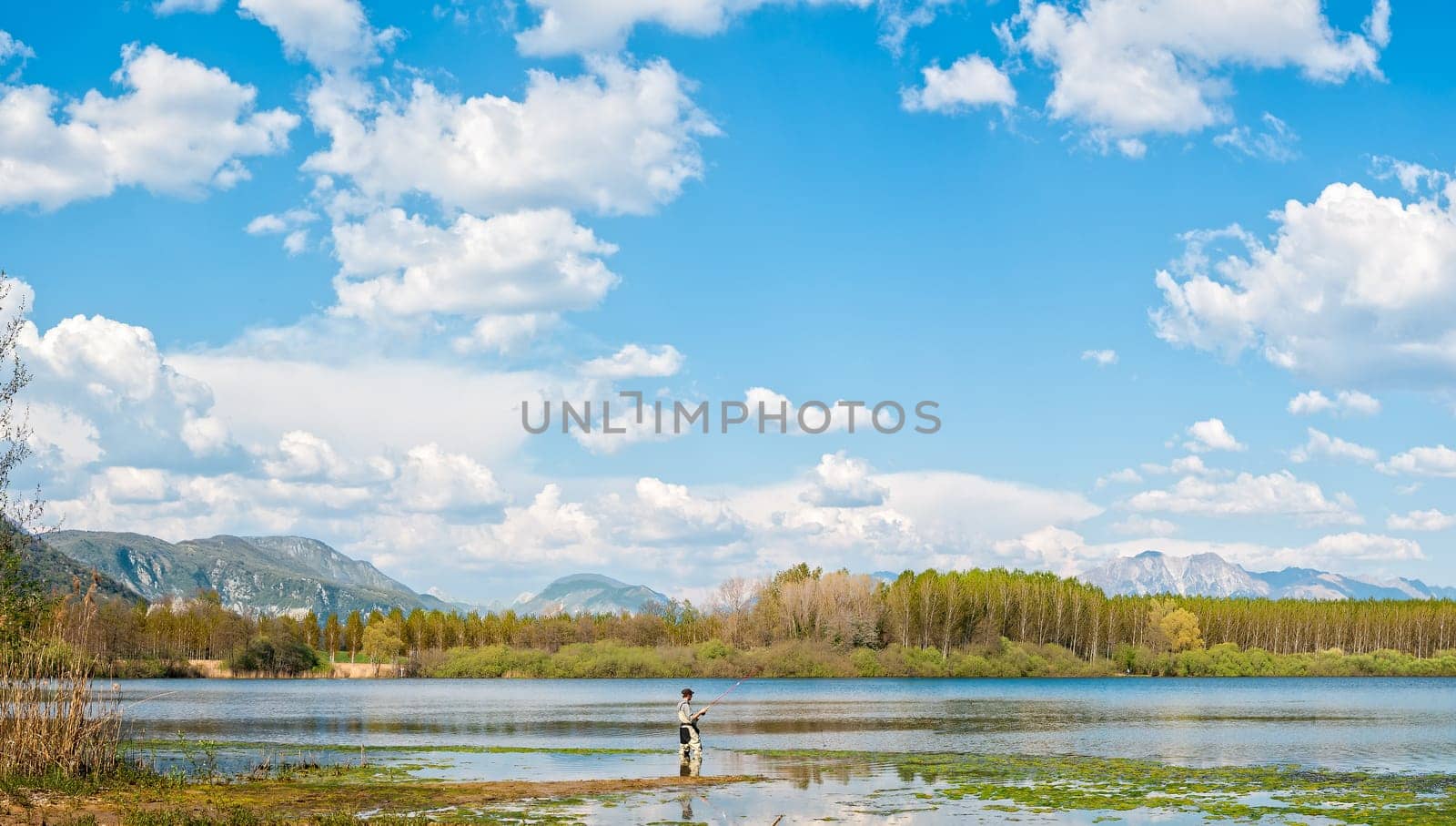 Man fishing from the shore of lake . Landscape with lake,forest,blue sky and cloud.