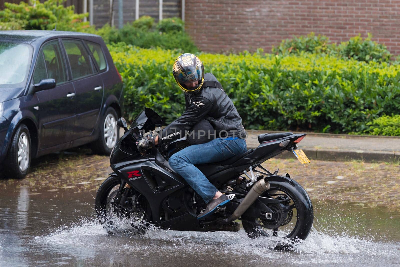 OLDENZAAL, NETHERLANDS - JULY 21, 2016: Unknown motor driver with his motor bike in a flooded street after a heavy rain