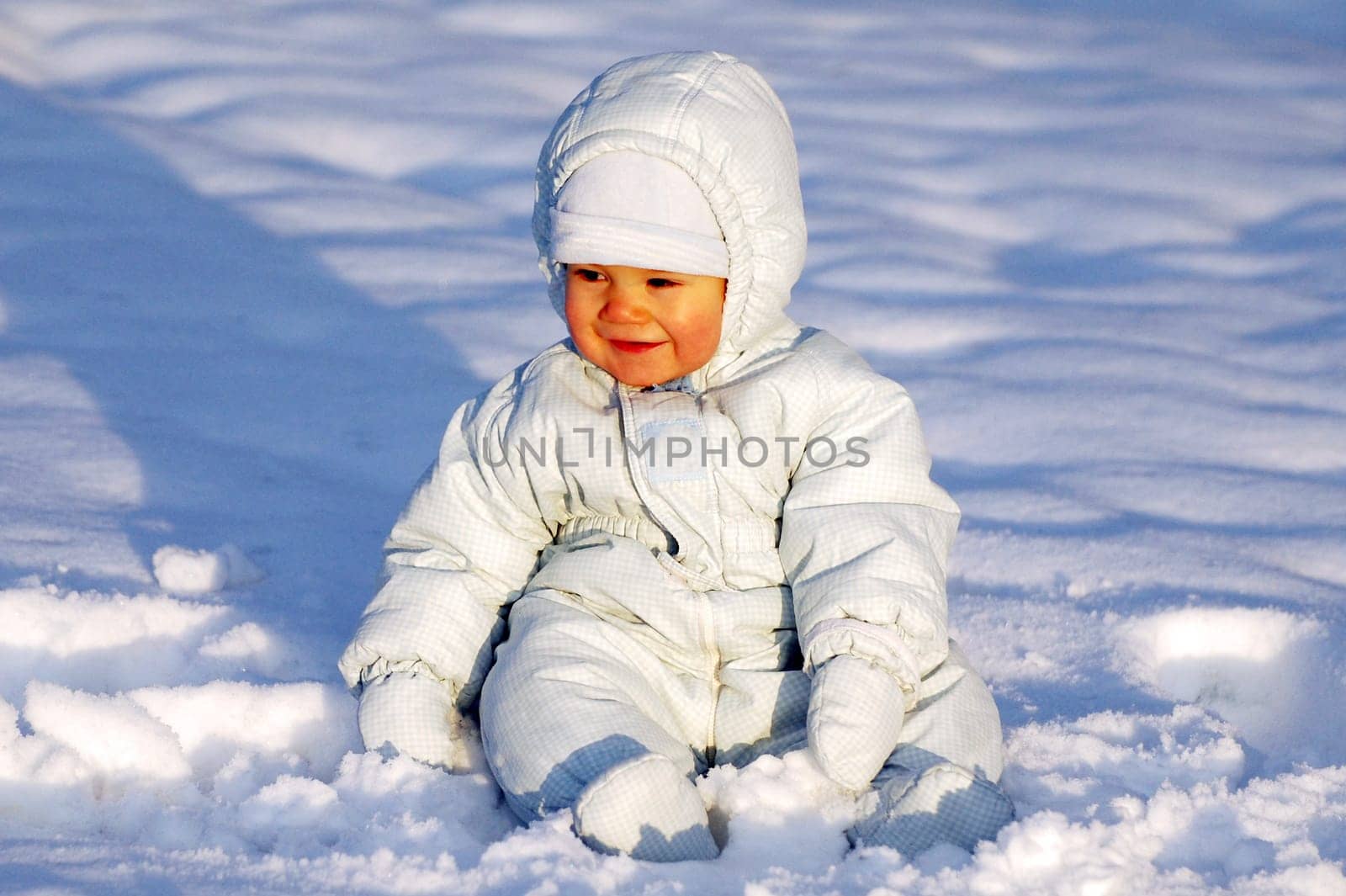 Happy smiling baby is sitting in the snow.