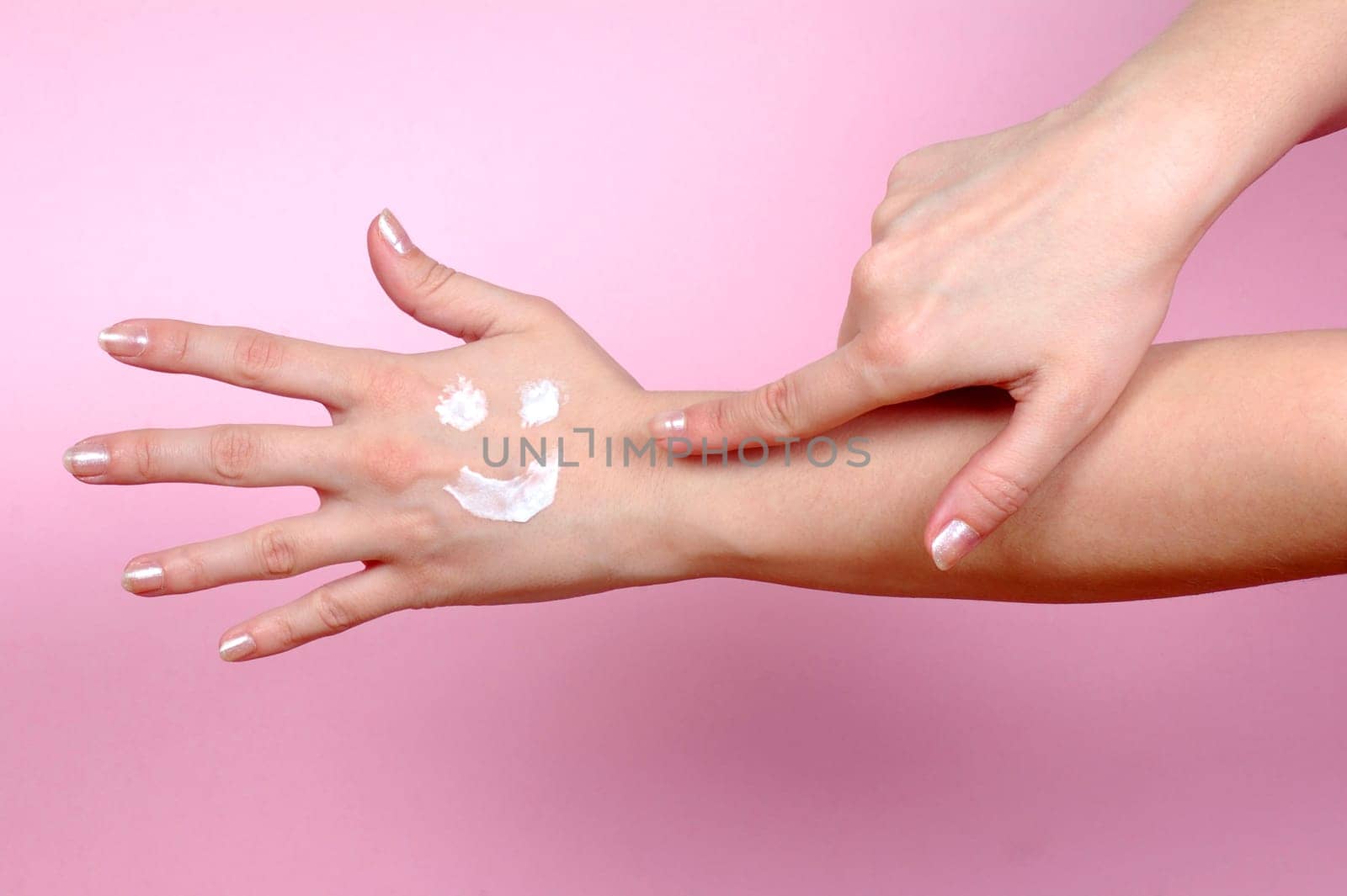 Hand shows to another hand where is smiley from hand cream. Skincare concept.