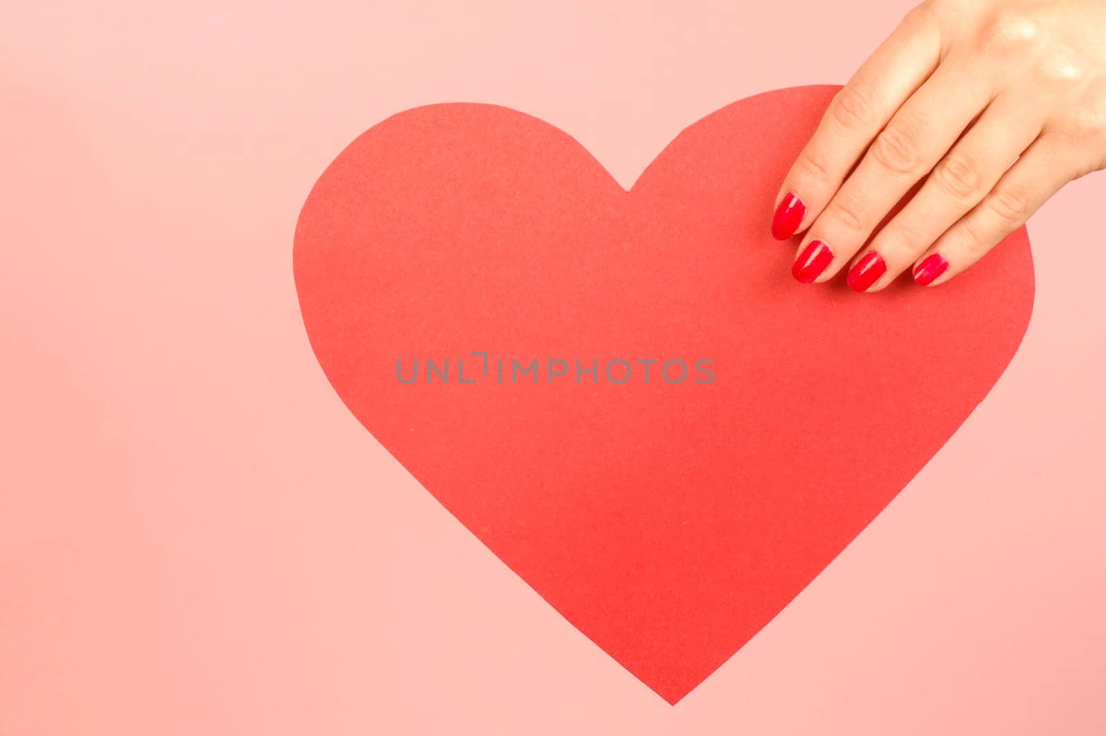 Red heart from paper in hand on red background.