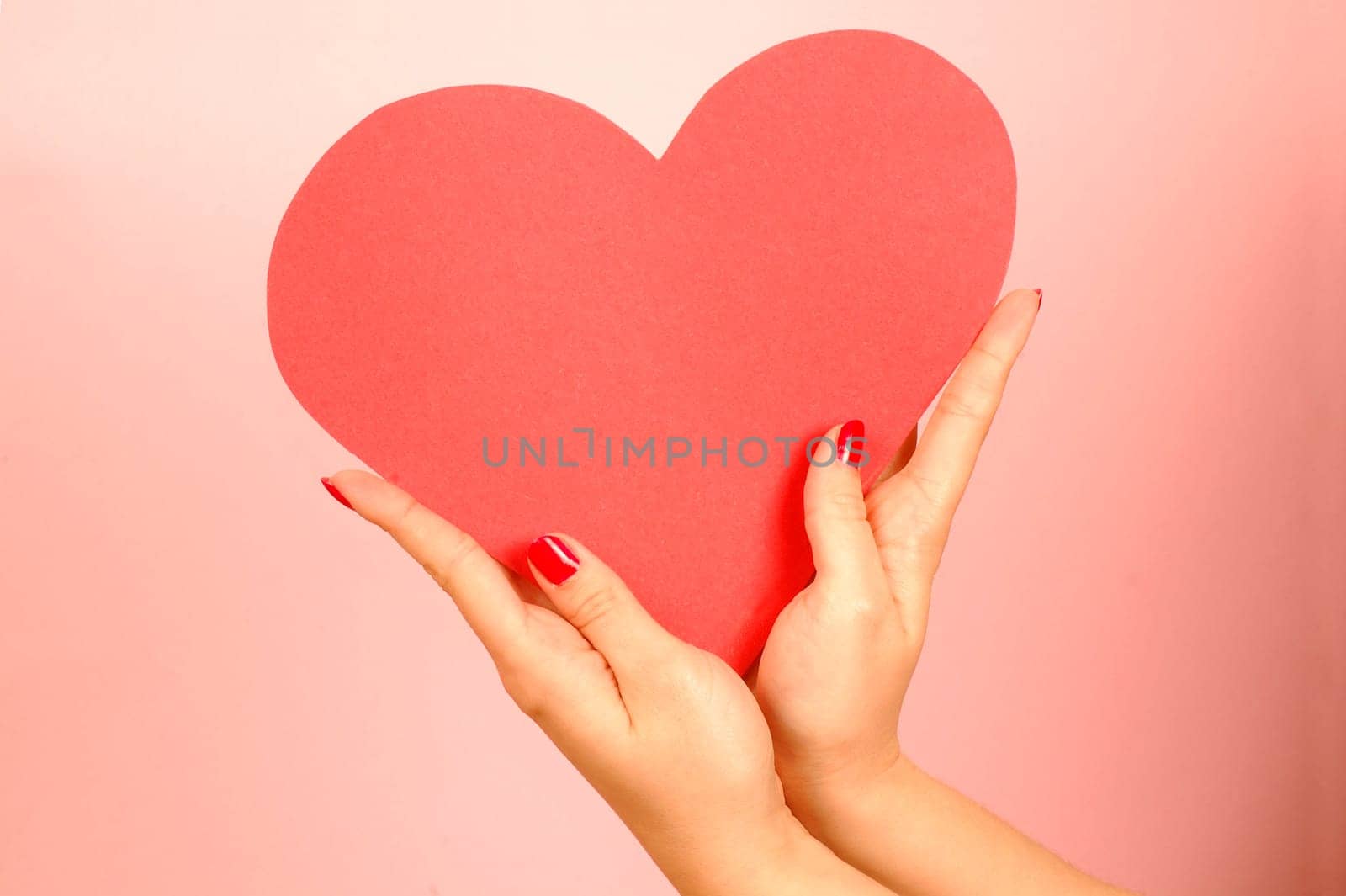 Red heart from paper in hands on red background.