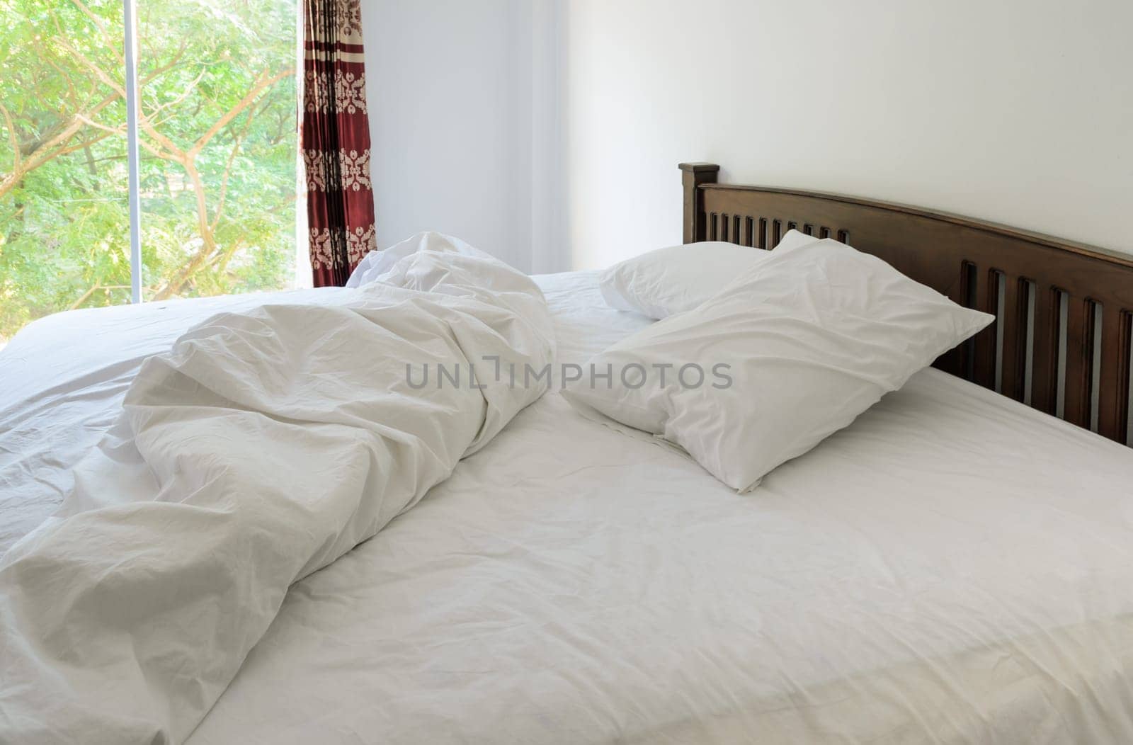 Morning view of an unmade bed in white bedroom with open curtain window