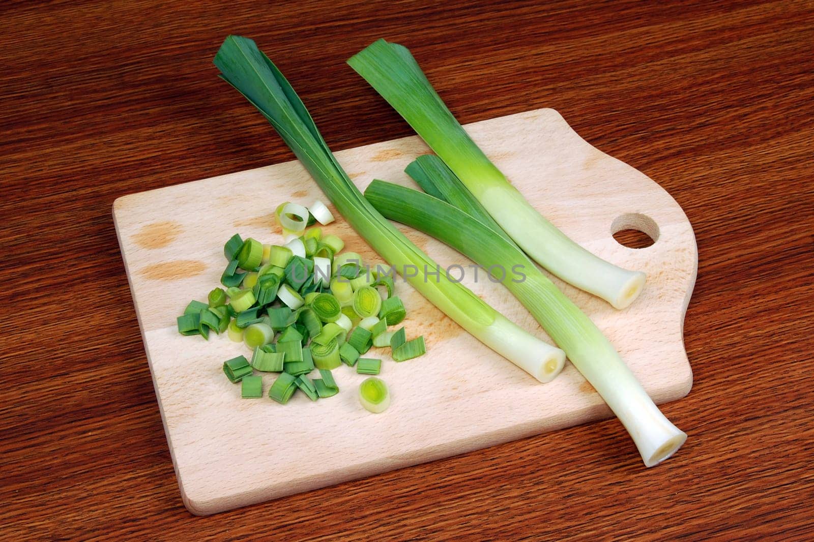 Leeks and slices are on cutting board on wooden table.