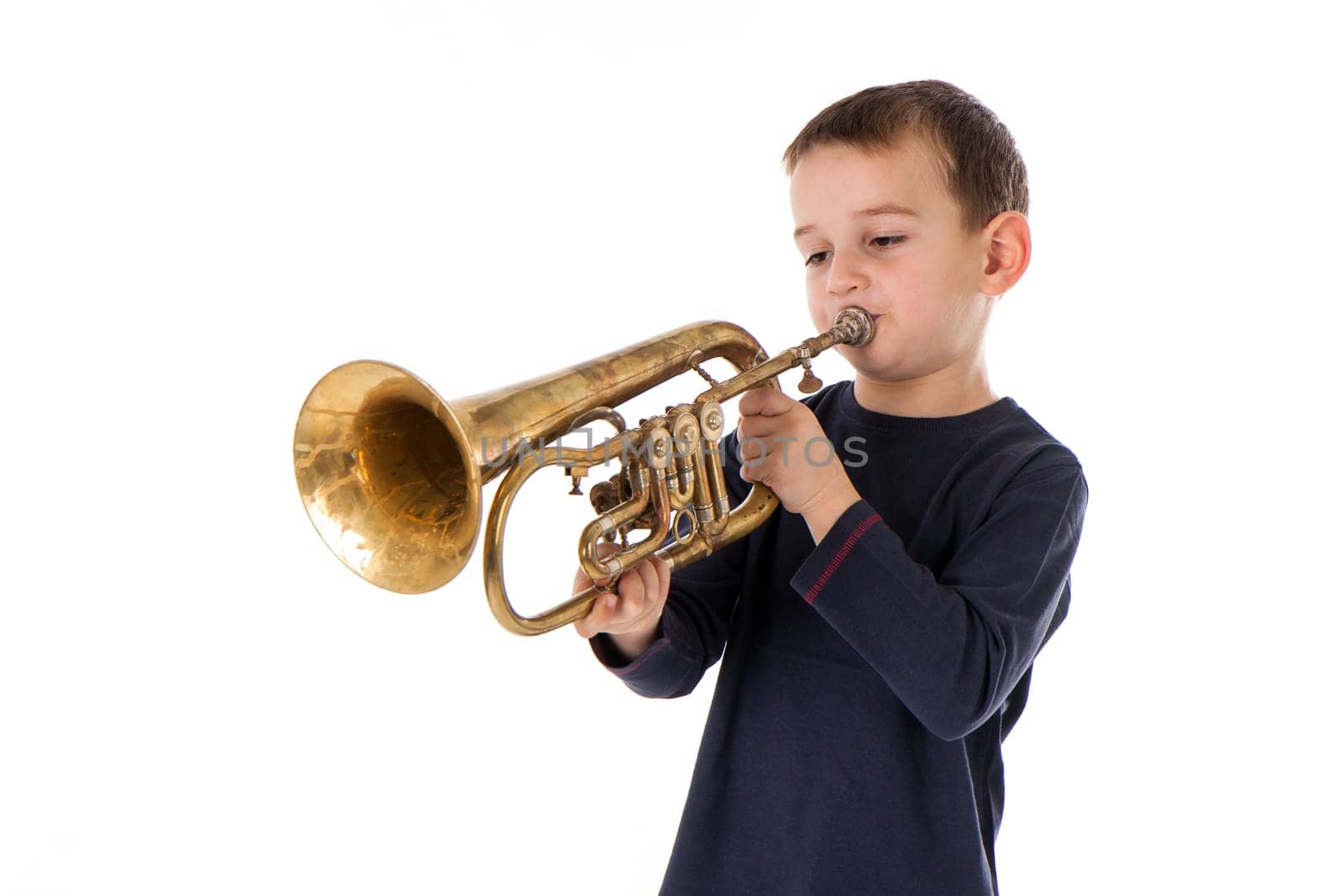 young boy blowing into a trumpet against white background