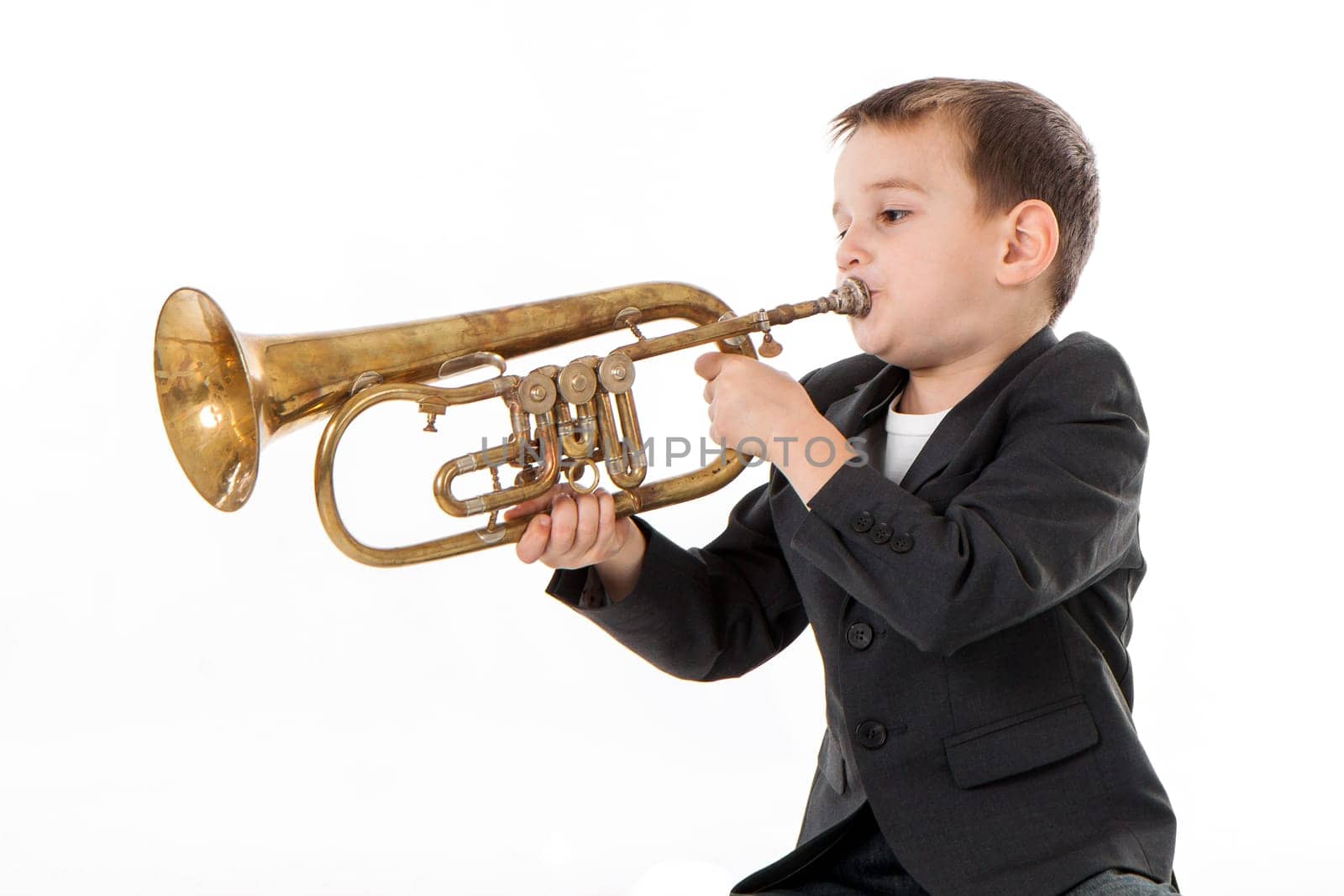 young boy blowing into a trumpet against white background