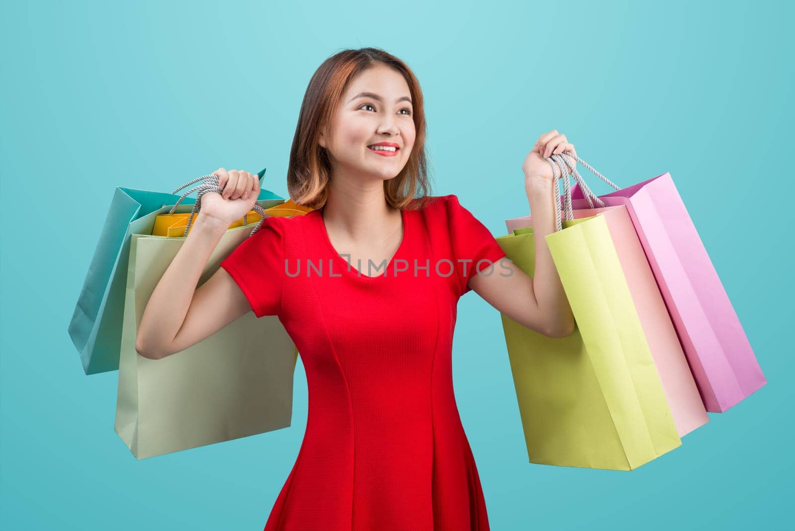 Beautiful young asian woman with colored shopping bags over blue background