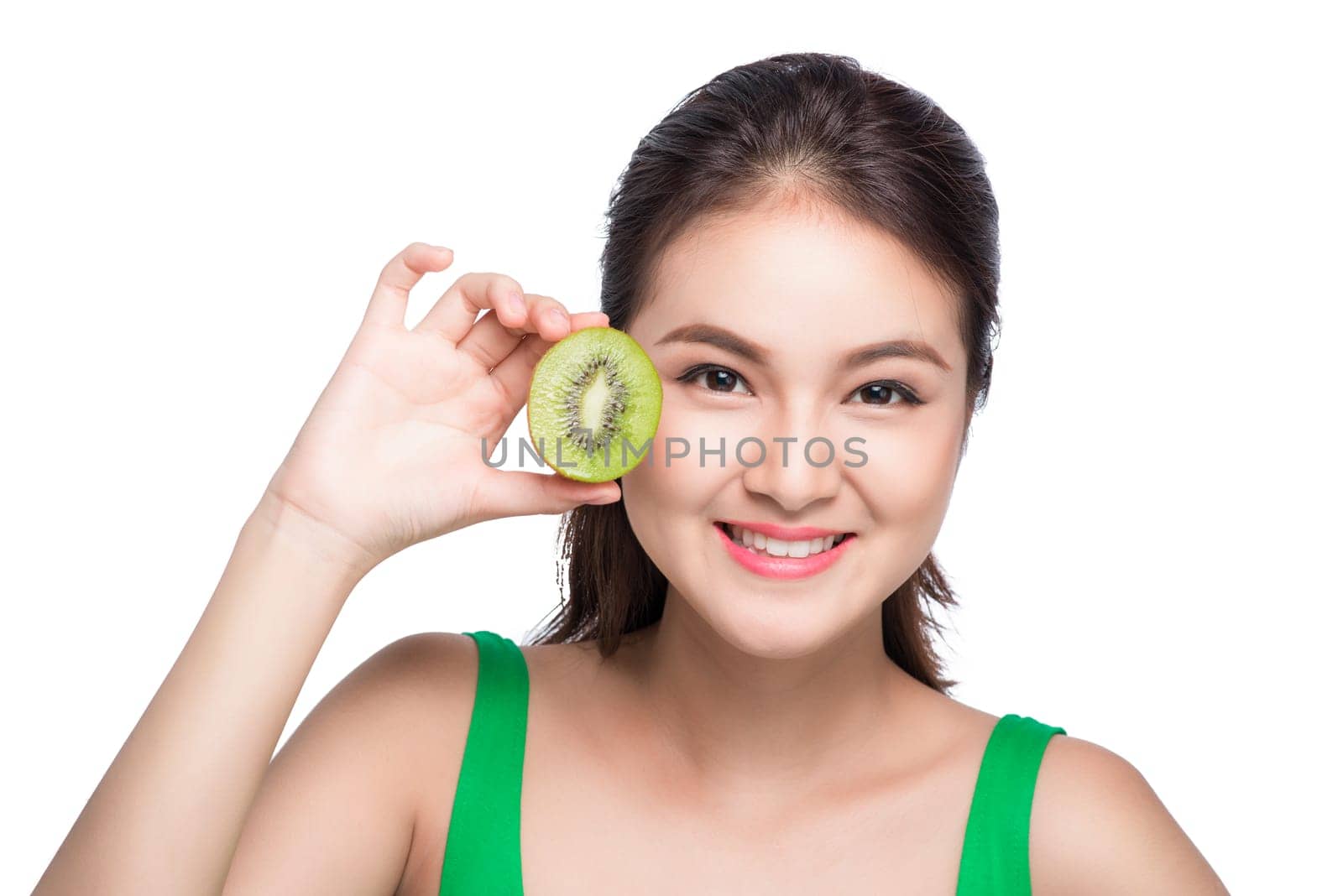 Tropical fruits. Healthy eating. Charming young asian woman holding fresh juicy kiwi and smiles. Green background.