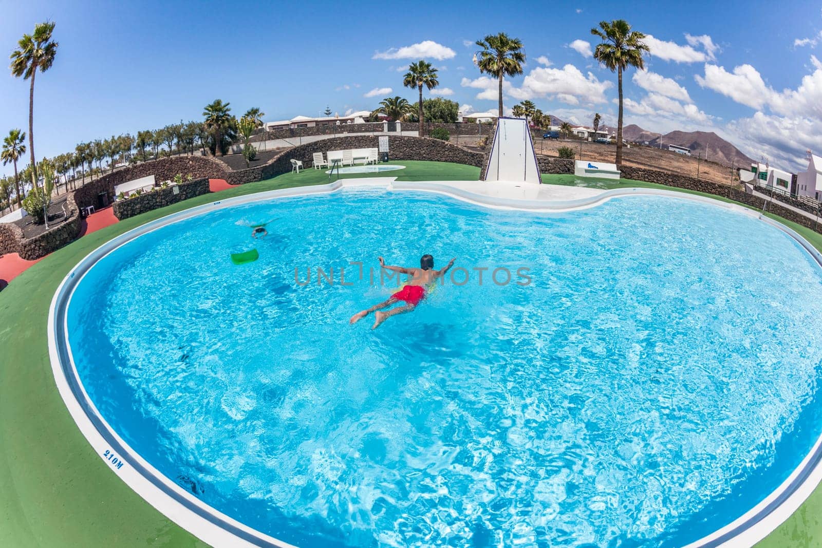 teenage BOY HAS FUN SWIMMING ON A SURF BOARD IN THE POOL
