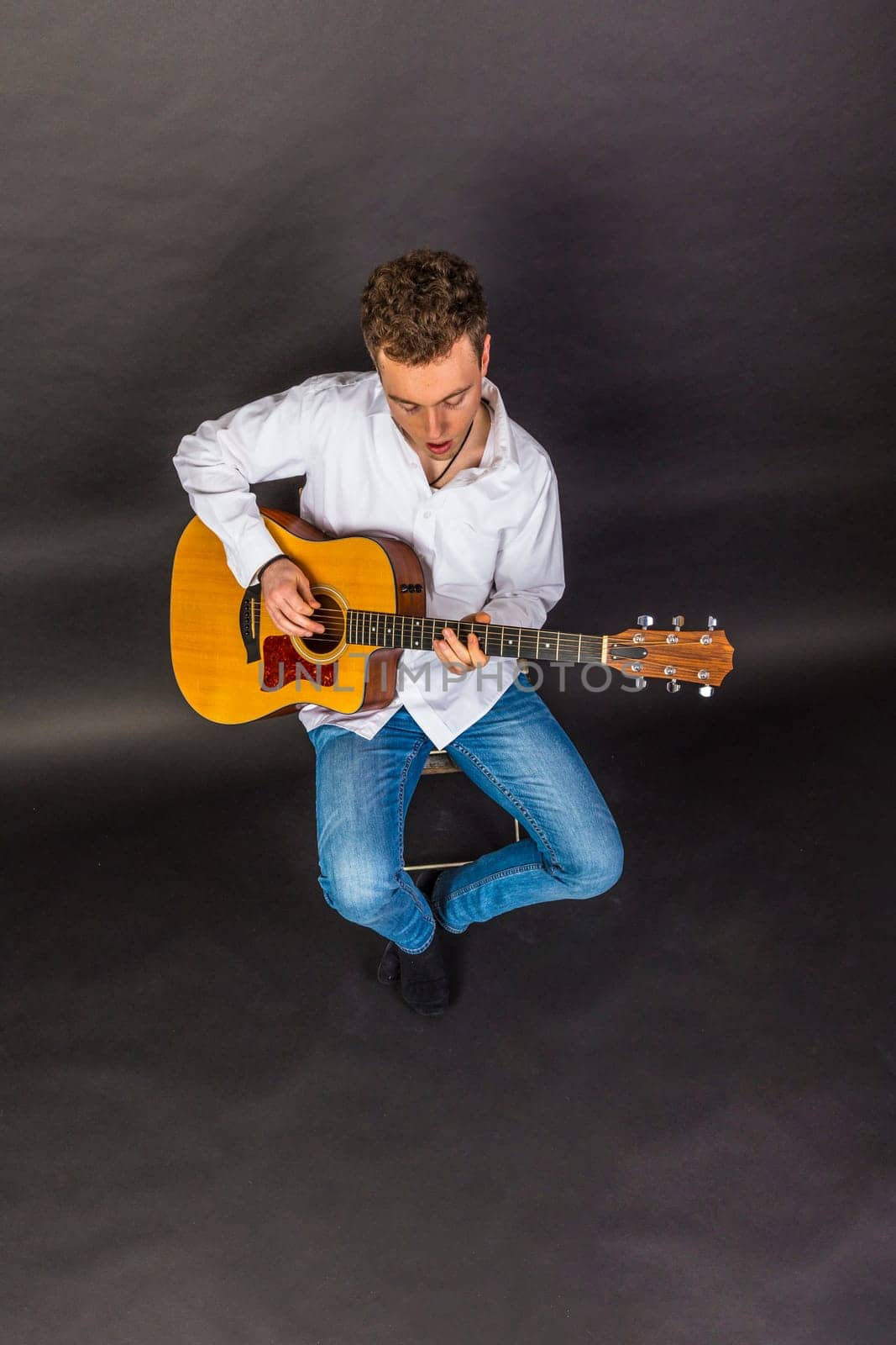 teenage guitar player sits on a chair and plays guitar