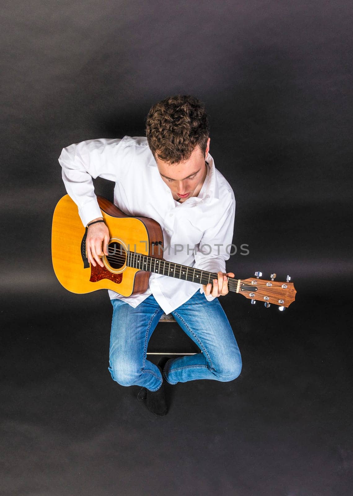 teenage guitar player sits on a chair and plays guitar