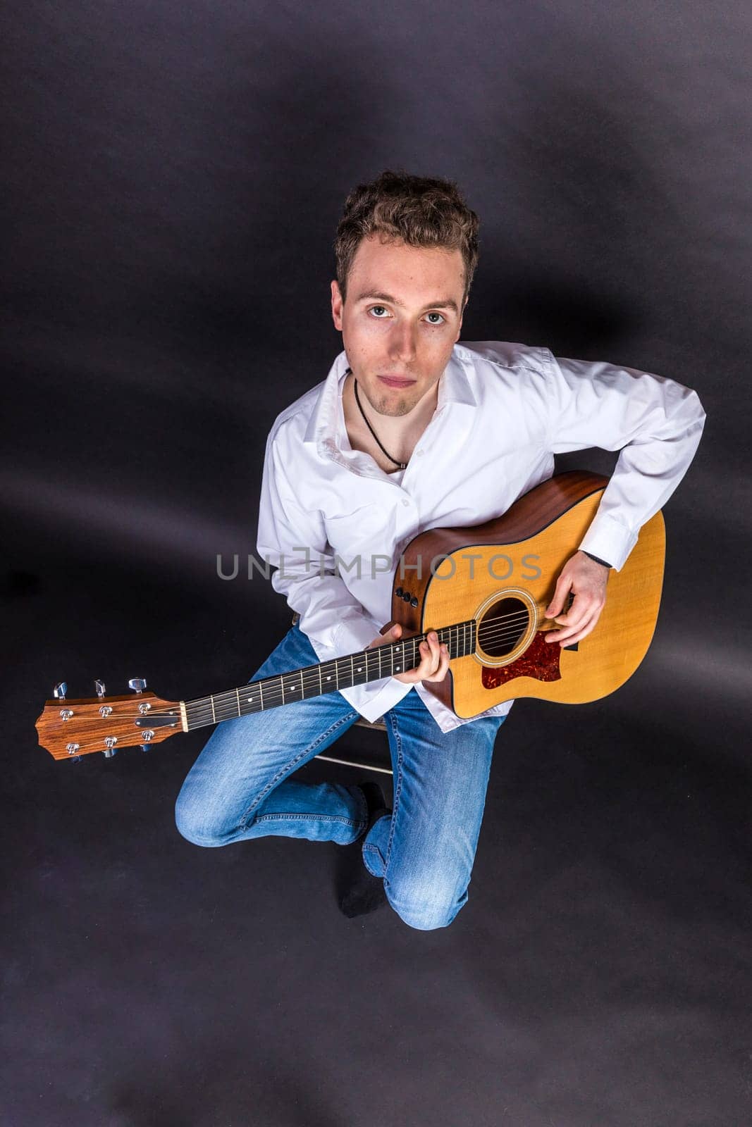 teenage guitar player sits on a chair and plays guitar