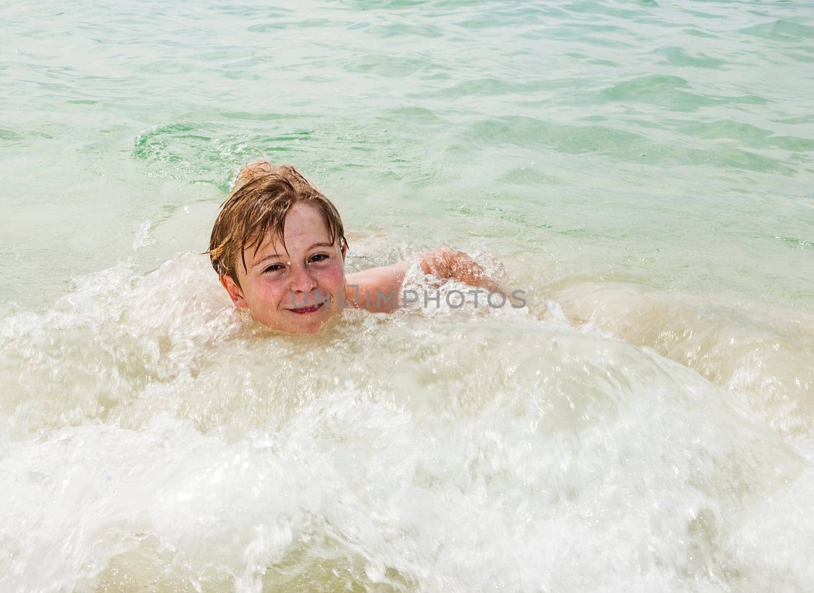 young happy boy with brown hair enjoys swimming in the beautiful sea