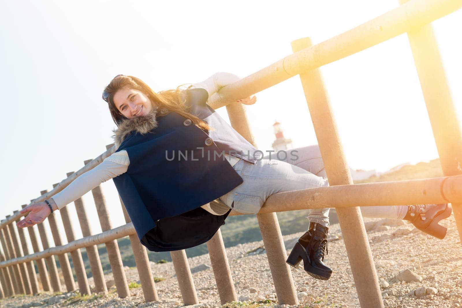 Beautiful happy young girl posing outdoors at sunset near a lighthouse