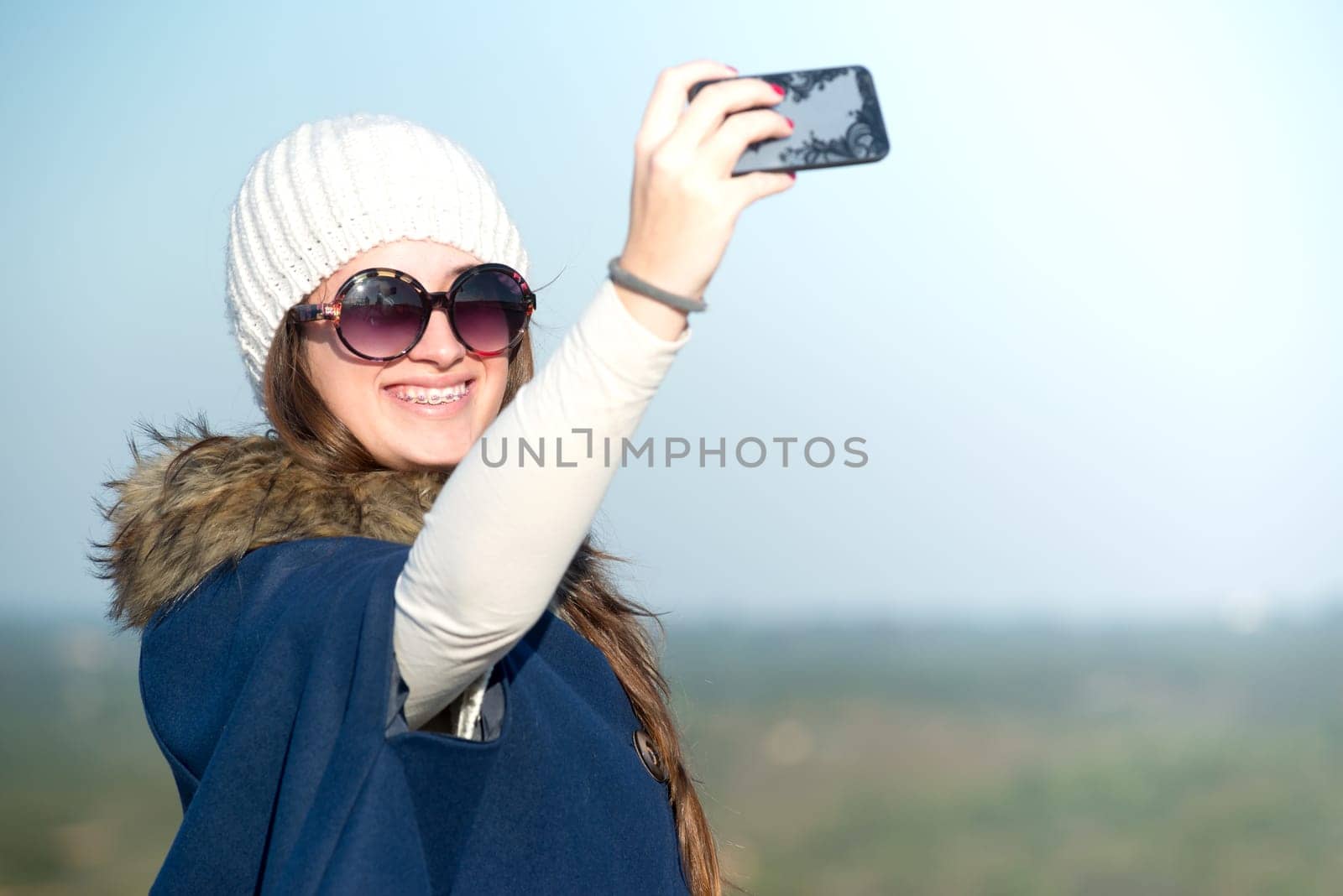 Beautiful happy young girl posing outdoors with phone taking a selfie