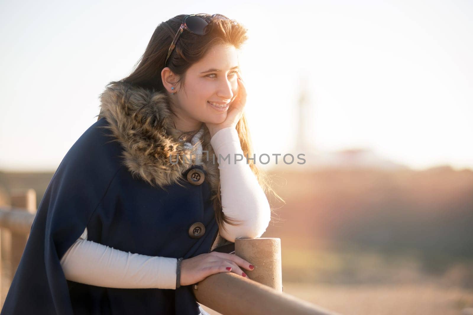 Beautiful happy young girl posing outdoors at sunset near a lighthouse
