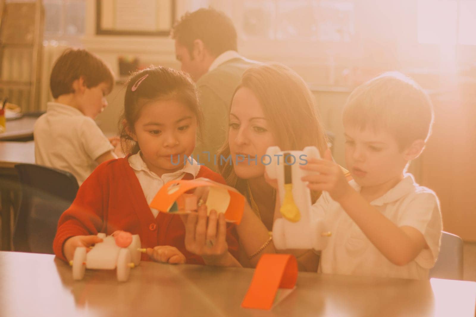 Primary school teacher is helping two of her students with a STEM project. They are building something using recycled items and crafts equipment.