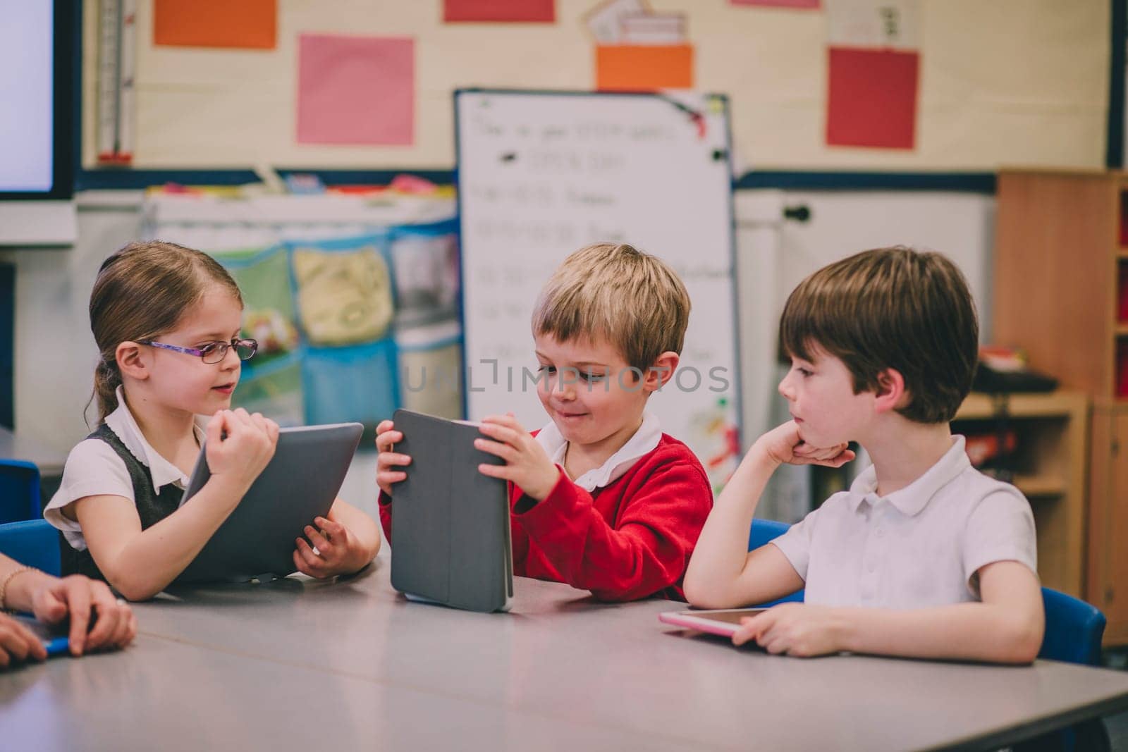 Table of primary school students in a classroom are using digital tablets to work on.