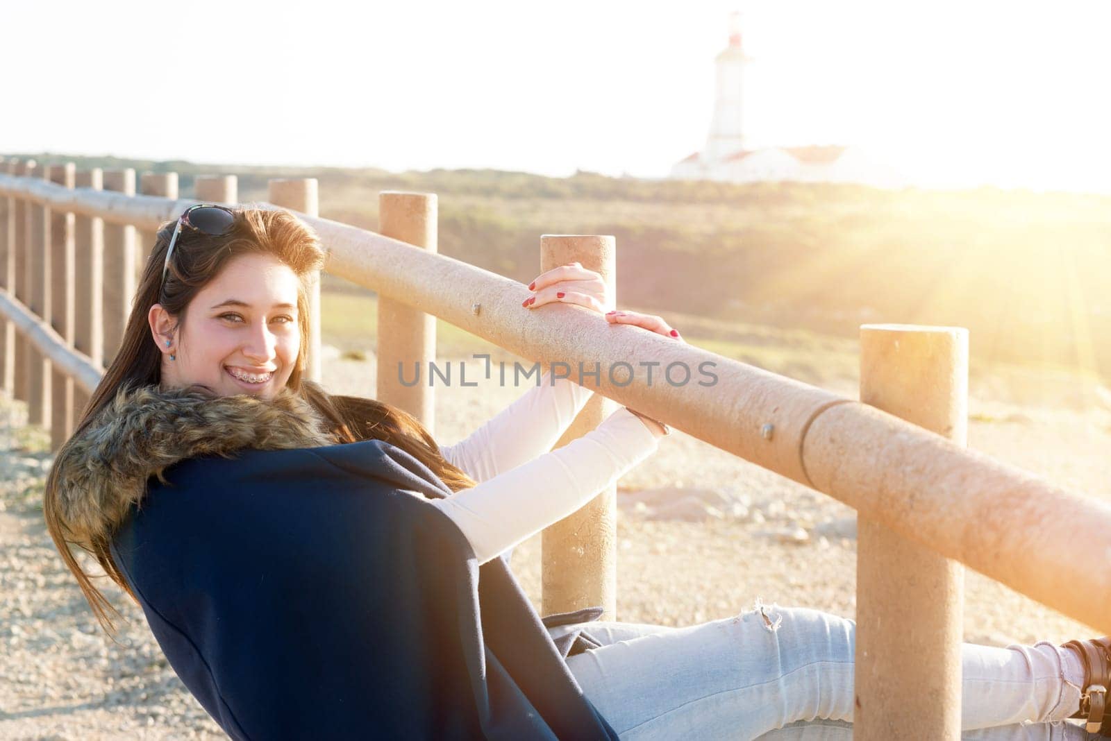 Beautiful happy young girl posing outdoors at sunset near a lighthouse