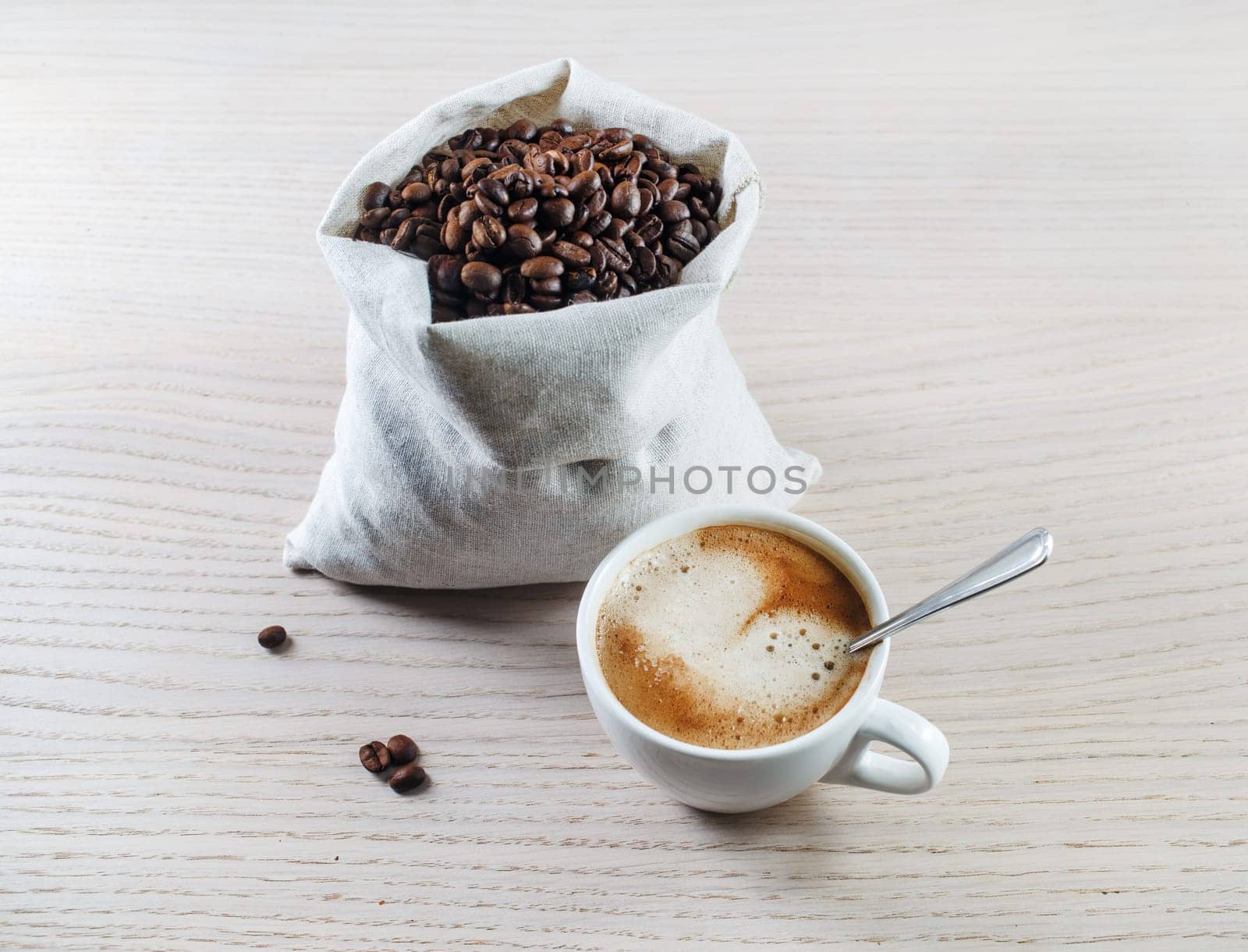 Espresso cup and coffee beans in a canvas bag against black wooden table background.