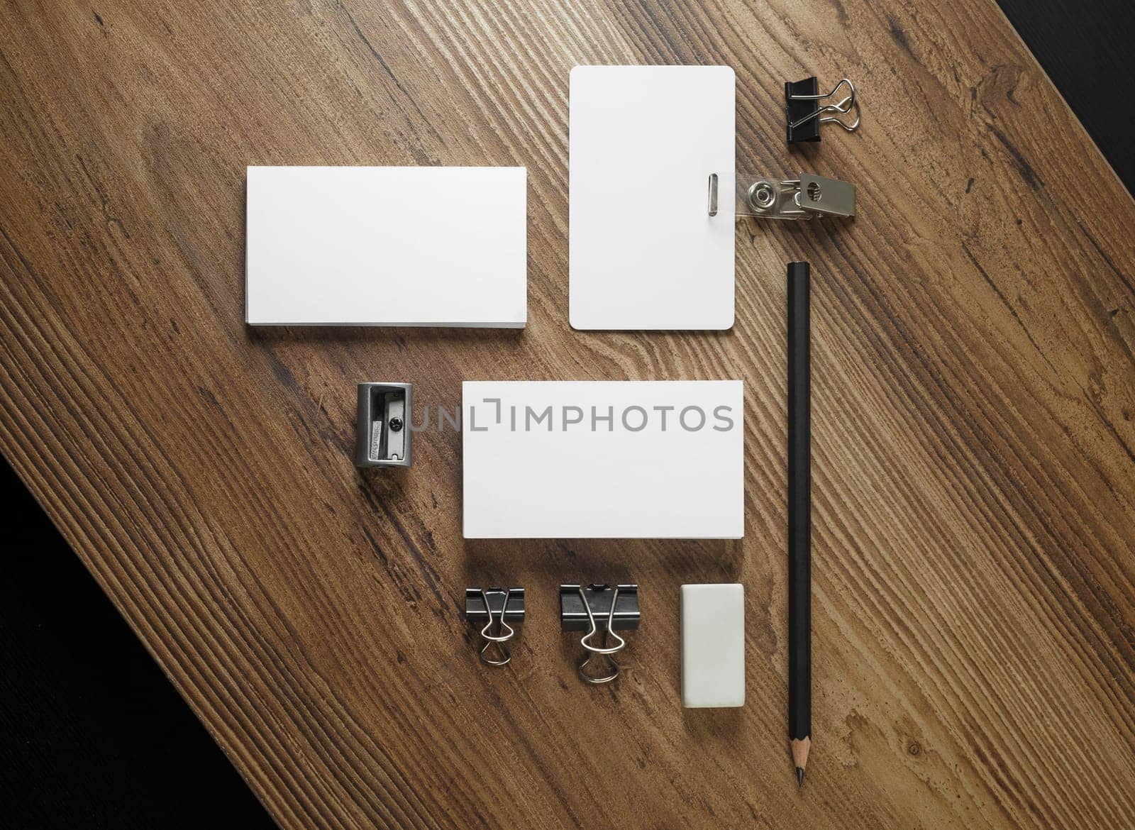 Photo of blank business cards, pencil, eraser, badge and sharpener on wooden table background. Blank stationery set. Mockup for your design. Responsive design template. Top view.