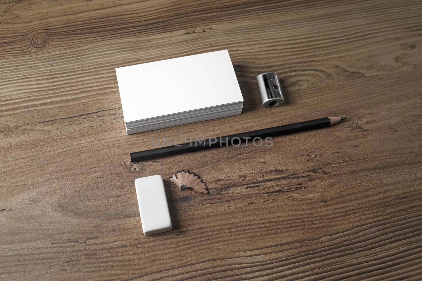 Photo of blank business cards, pencil, eraser and sharpener on wooden background. ID template. Mockup for branding identity for designers. Top view.