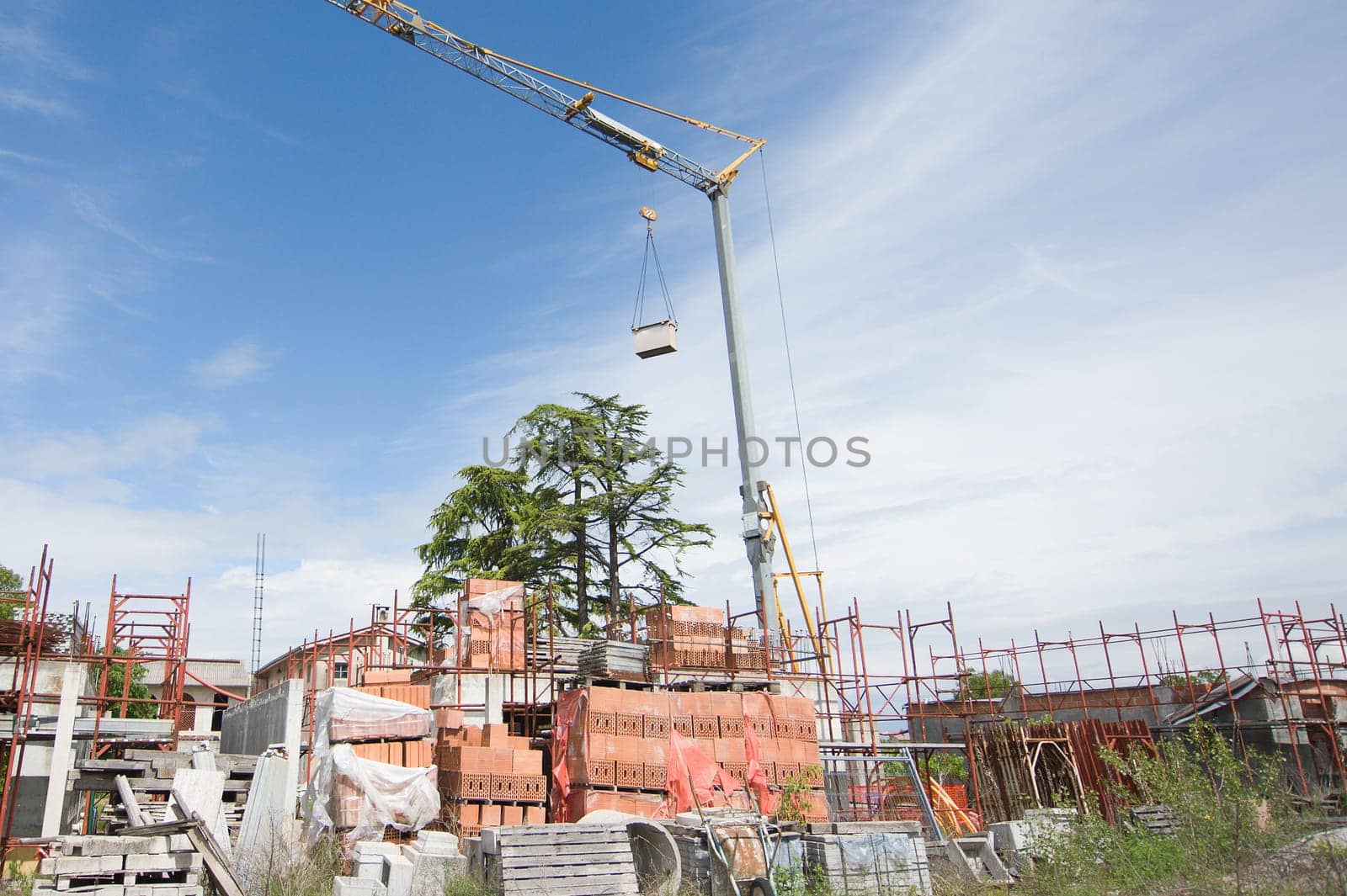 Small construction site with houses under construction. Construction cranes, scaffolding, bricks and other building materials.