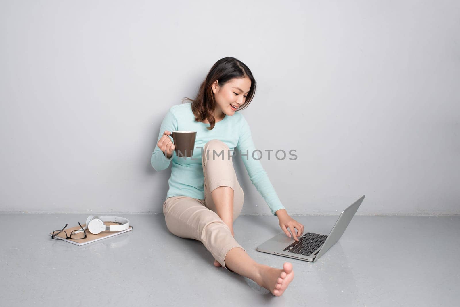 Happy casual beautiful asian woman working on a laptop sitting on floor at home.