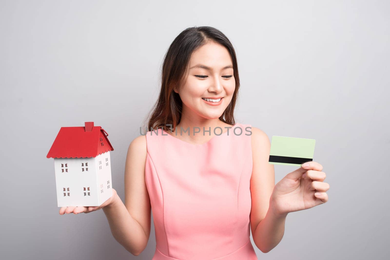 Invest in real estate concept. Woman holding small toy house and credit card in hands