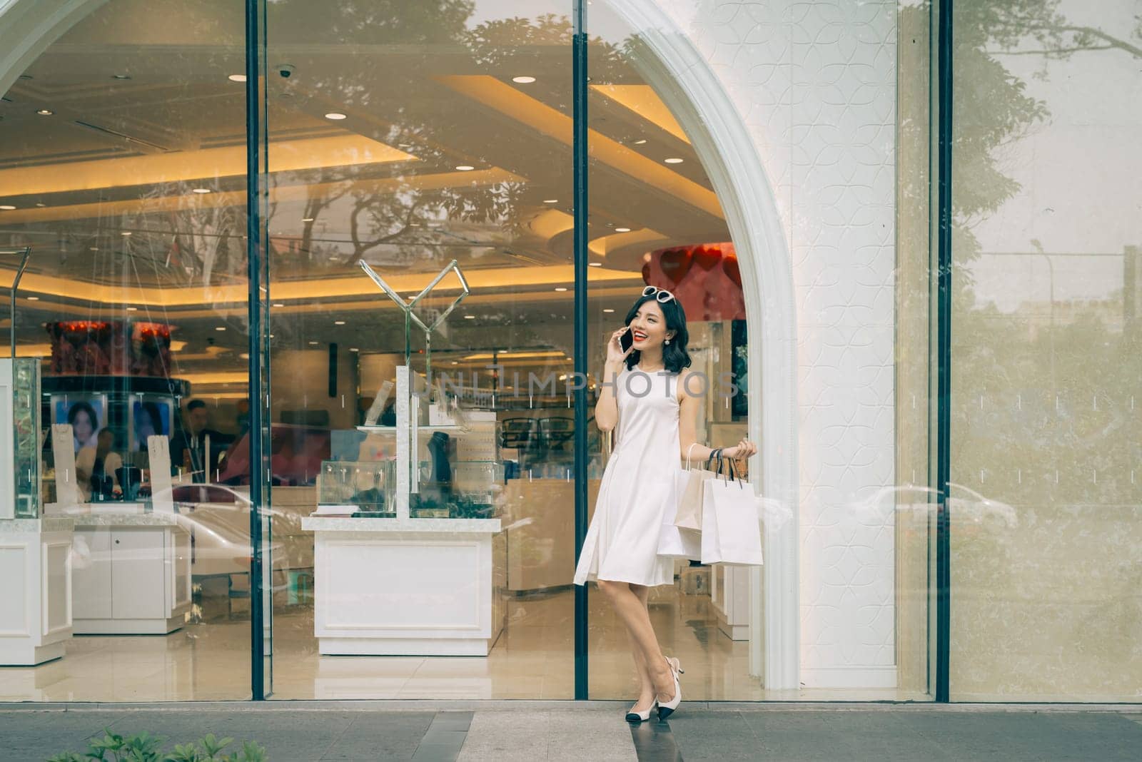Beautiful asian girl with shopping bags listening to mobile phone standing outside the mall