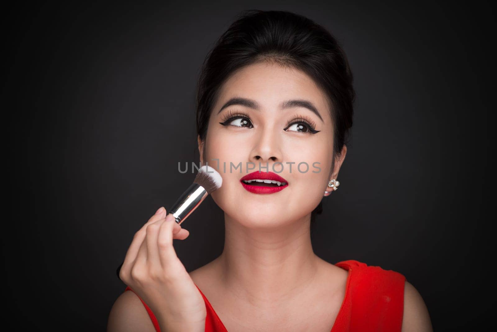 Cosmetic powder brush. Asian woman applying blusher on her cheeks with perfect make-up and red lips