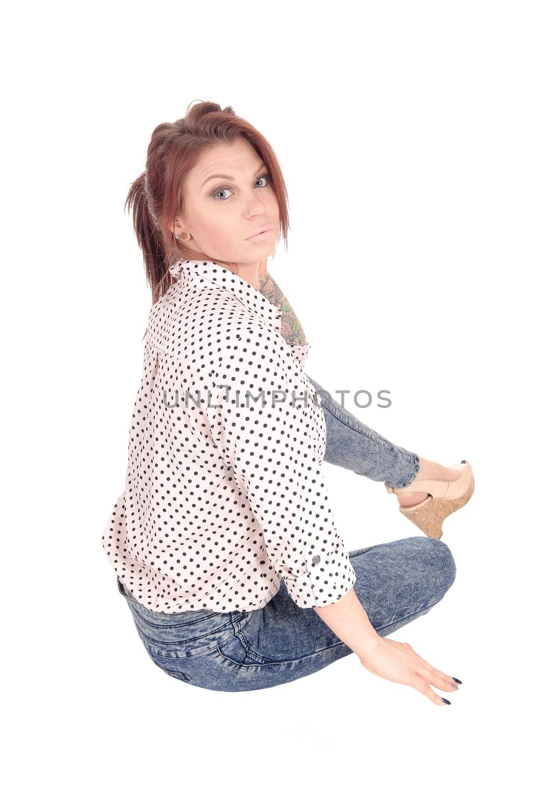 A beautiful young Caucasian woman sitting on the.floor in jeans and blouse, looking up, isolated for white background..