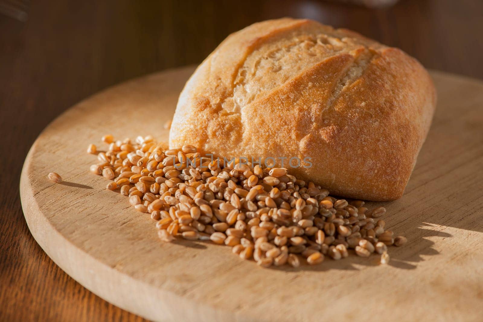 Single roll with spelt grains in front of it on a round breakfast board in the side light.