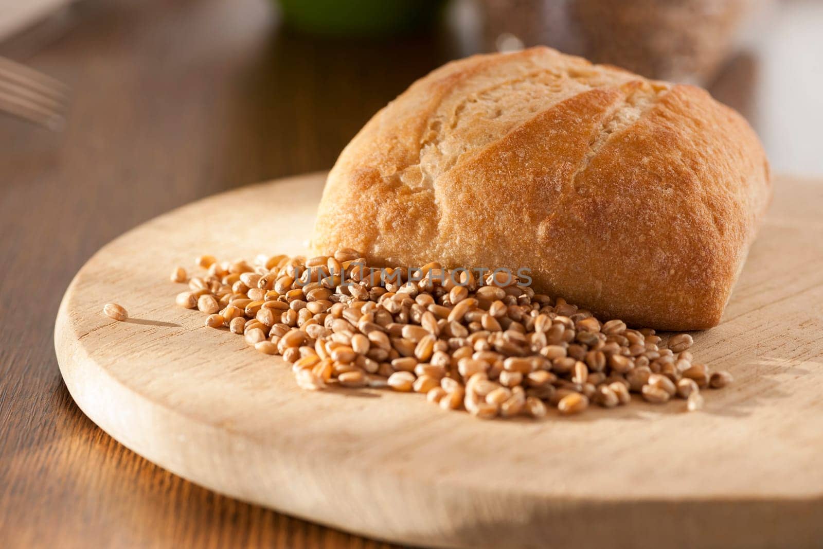 Single roll with spelt grains in front of it on a round breakfast board in the side light.