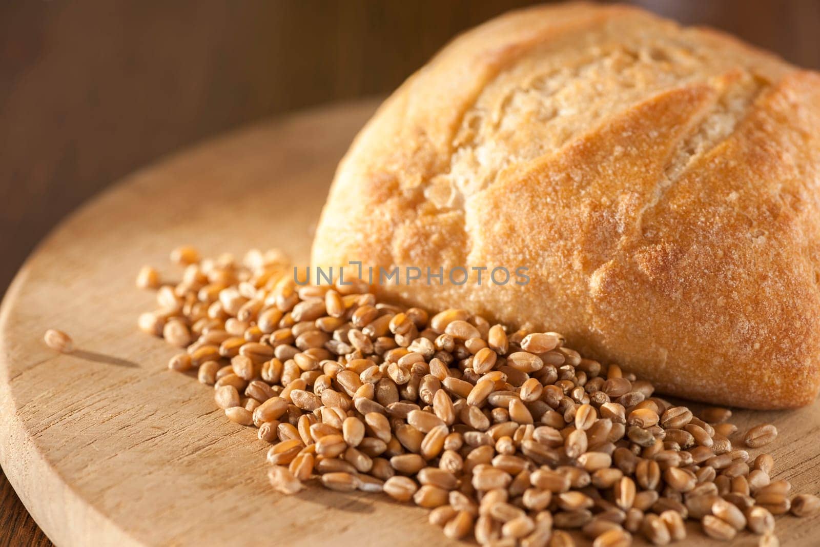 Single roll with spelt grains in front of it on a round breakfast board in the side light.