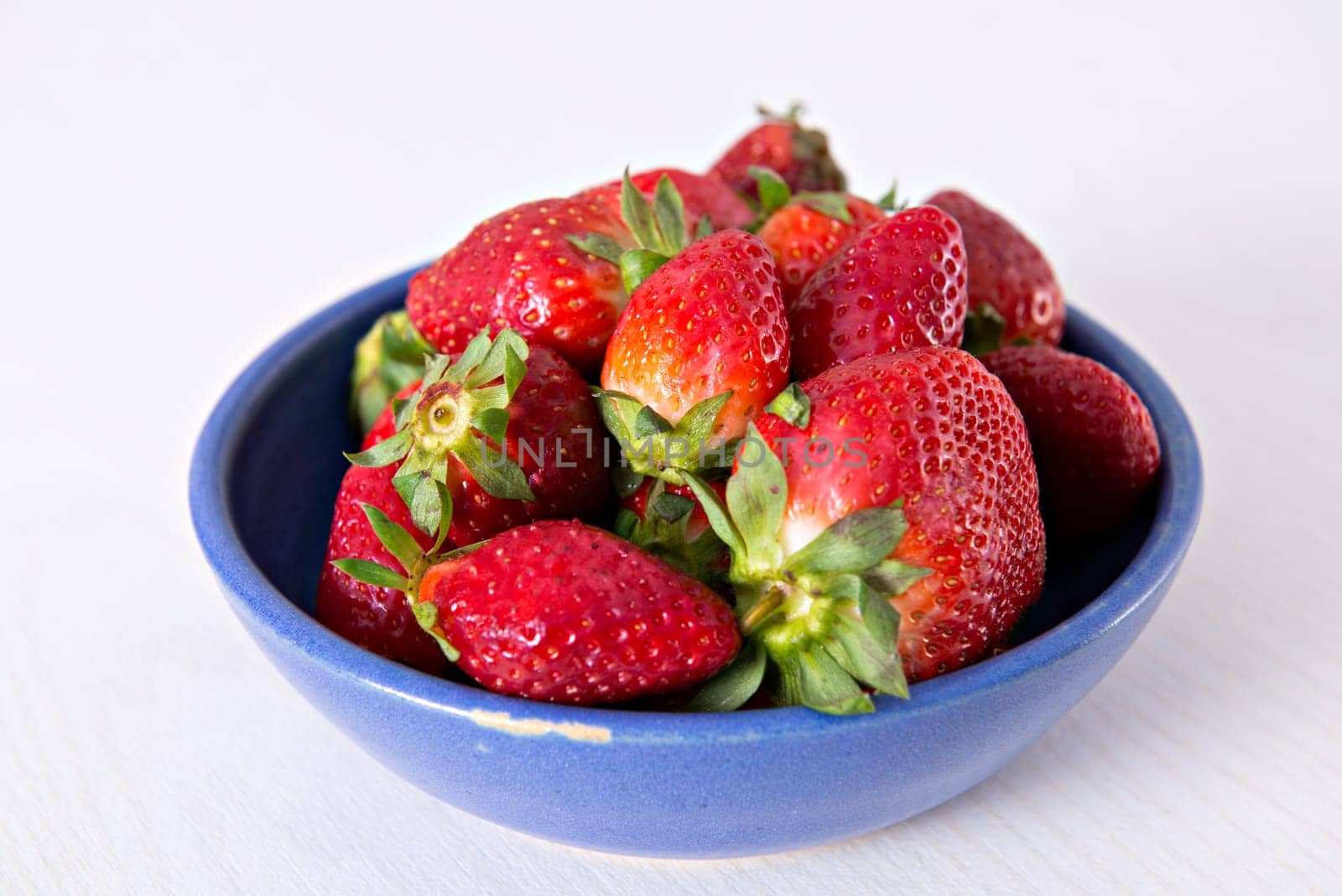 strawberries in blue bowl on white ground