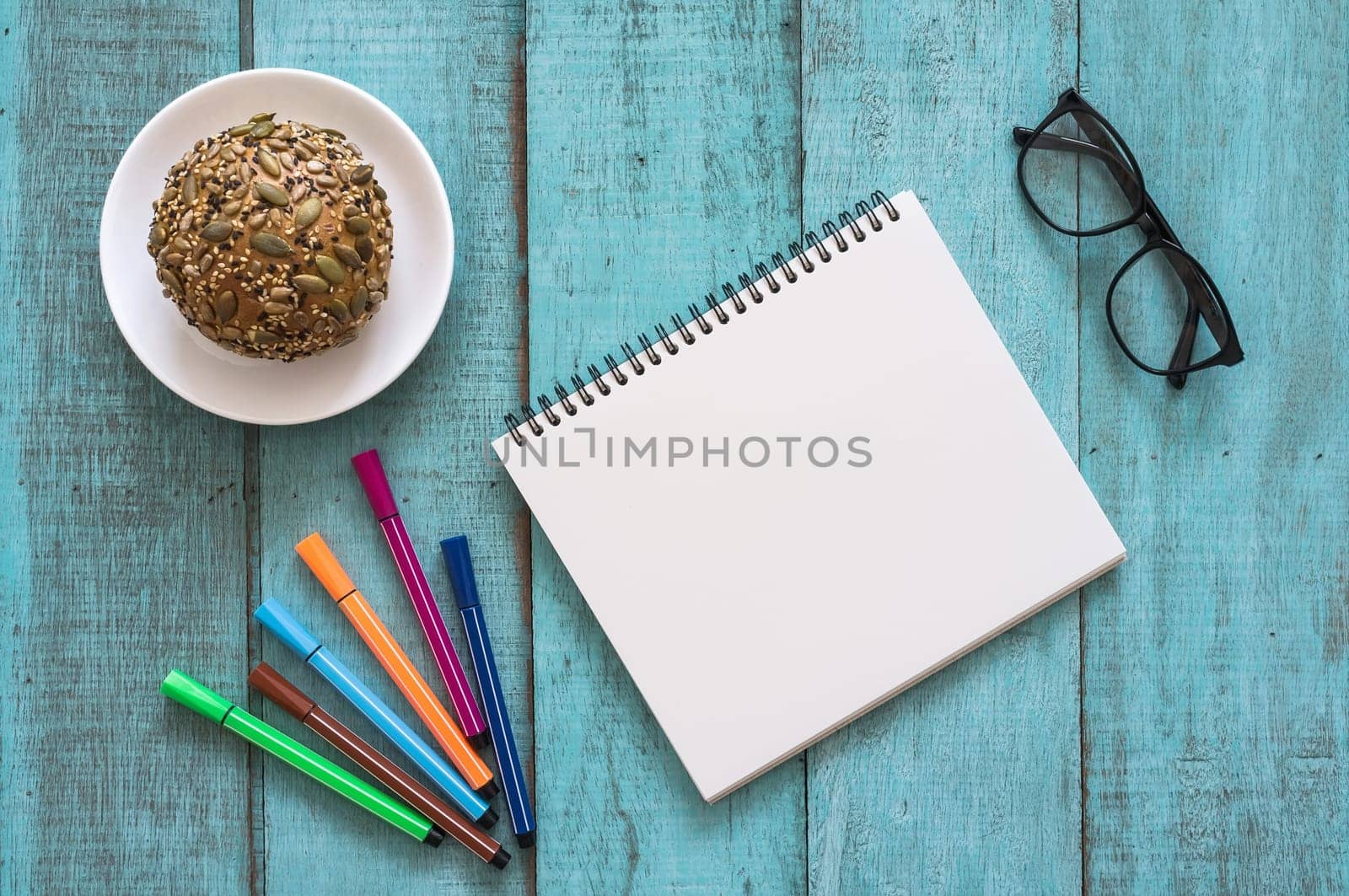 Blue wooden desk table with notebook, color pen, bread and cup of coffee. Top view with copy space, flat lay.