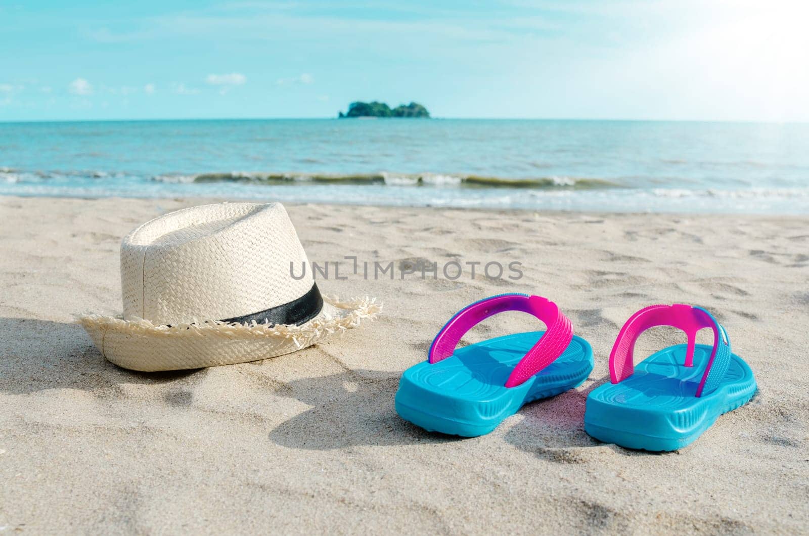 Straw hat and colorful flip flops on beach against sunny sky. Summer vacation concept.