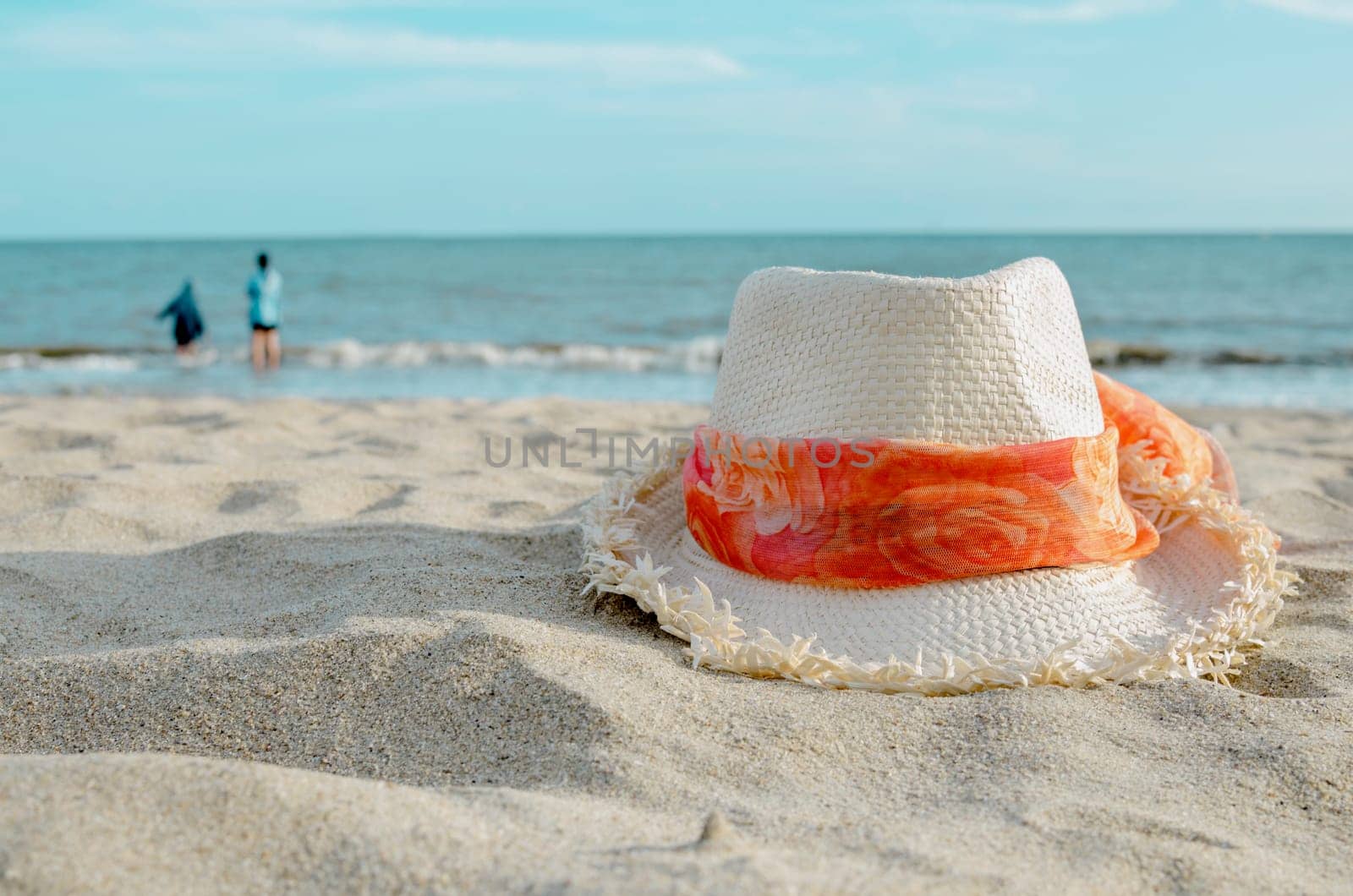 Straw hat on beach with blur people and sea background. Summer vacation concept.
