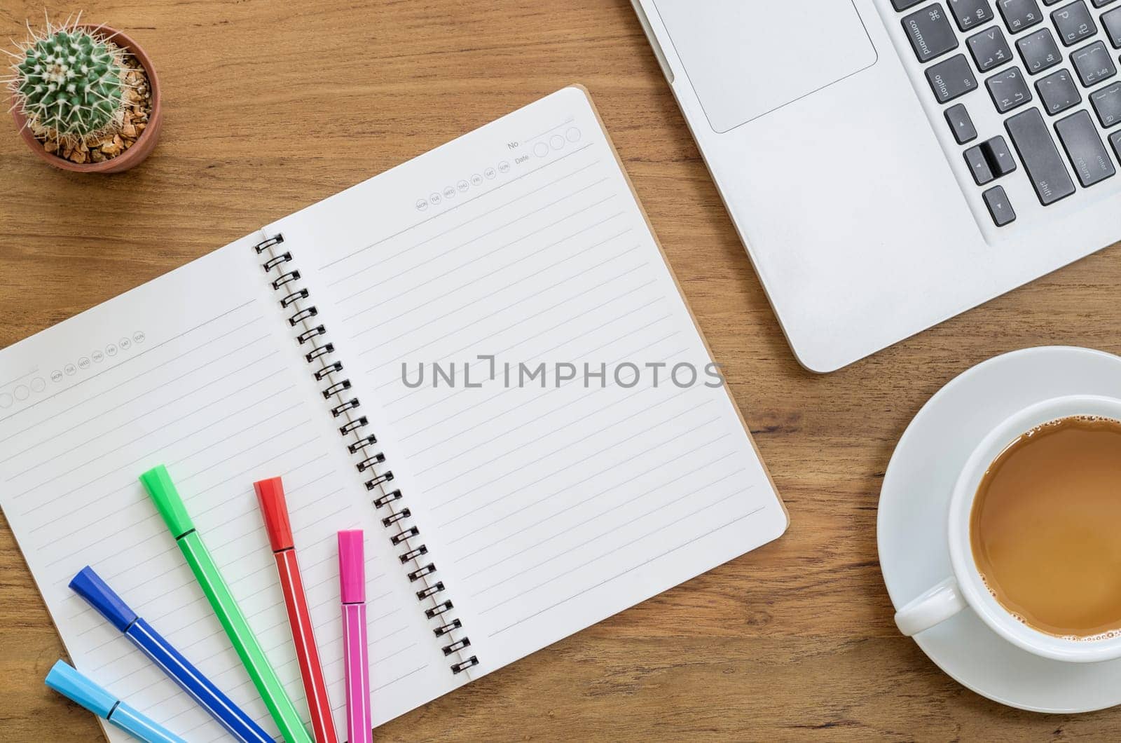 Wooden desk table with notebook, computer laptop, color pens, cactus and cup of coffee. Top view with copy space, flat lay.