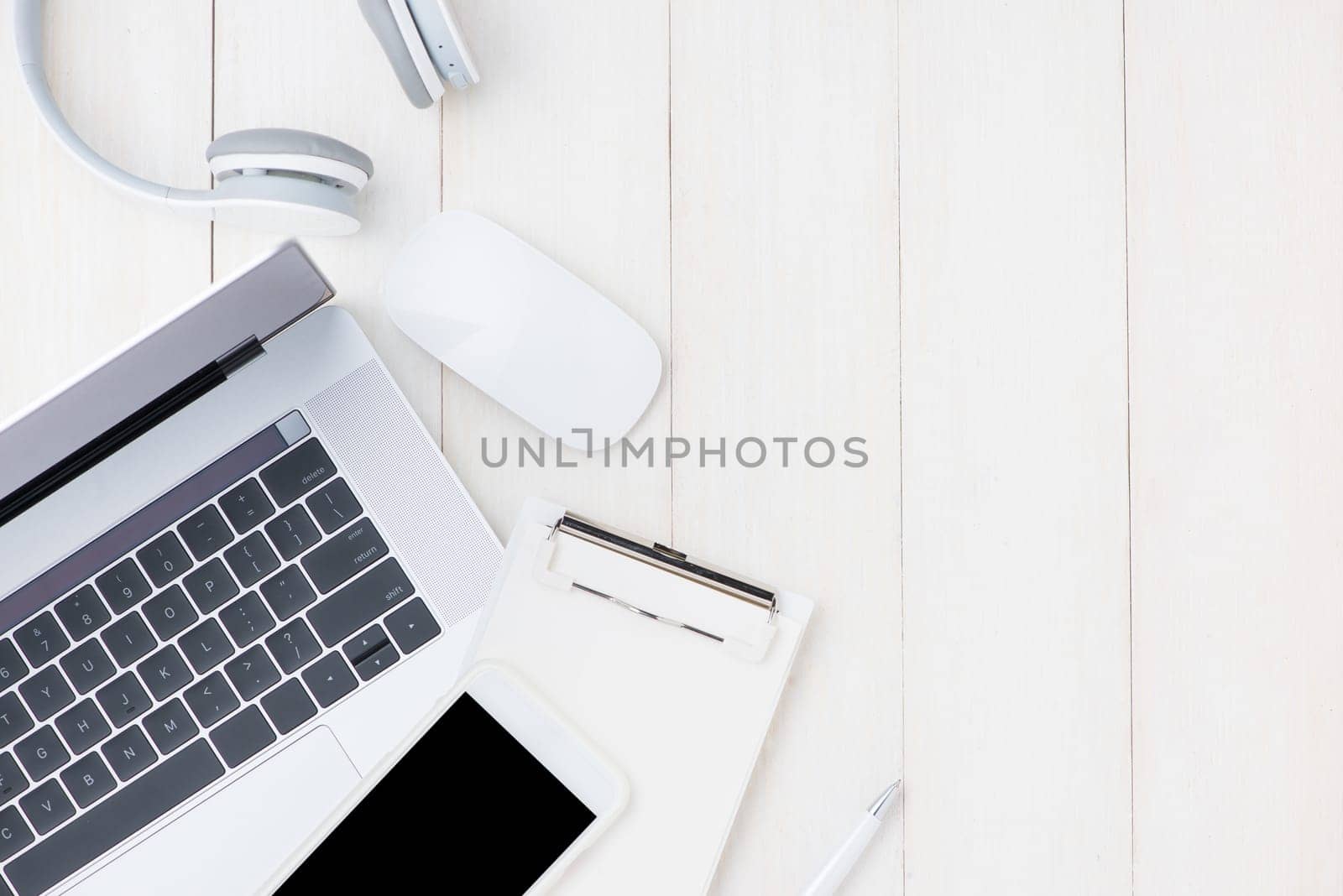 Laptop computer on white table with headphone and smartphone. View from above