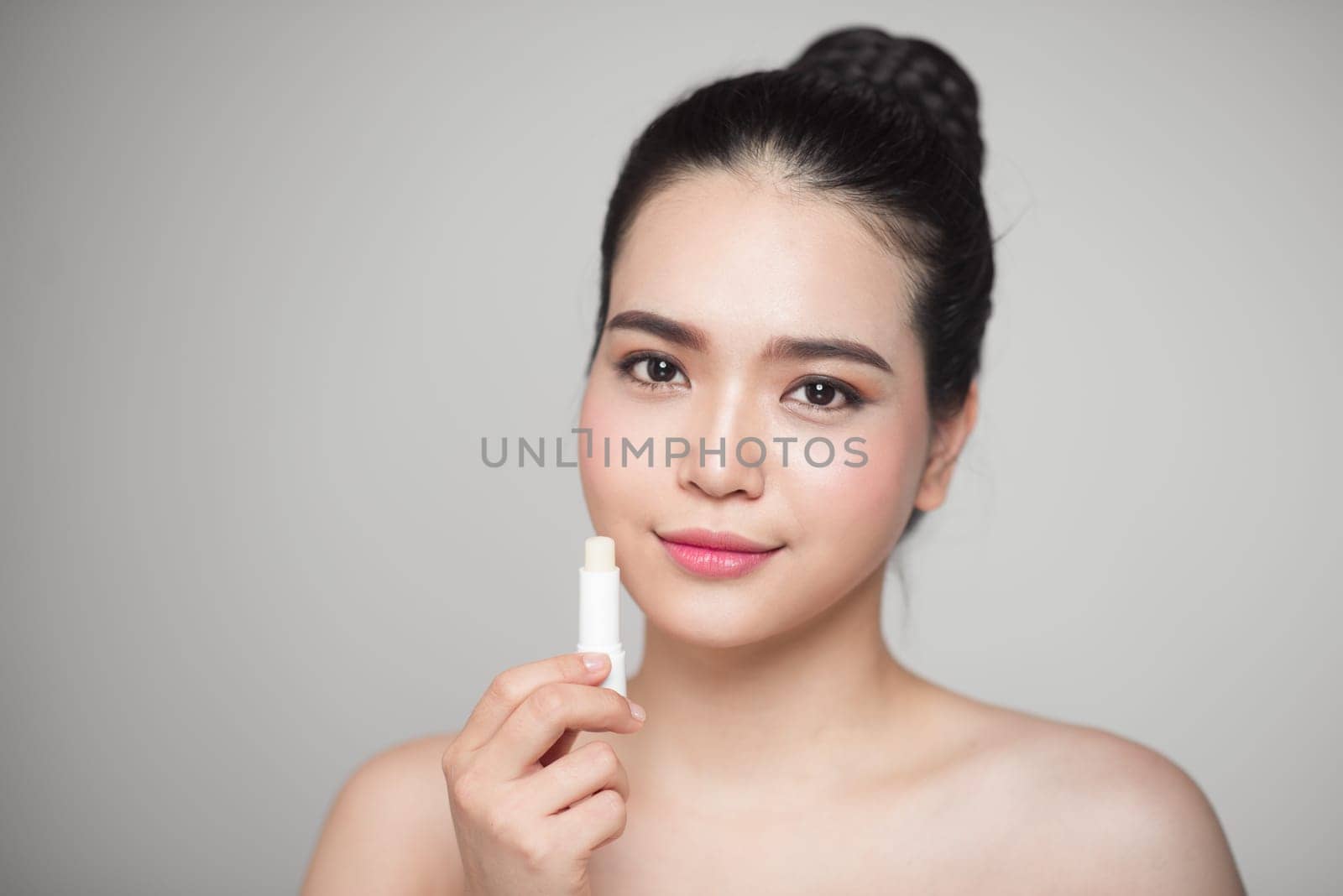 Asian woman applying hygienic lip balm over grey background