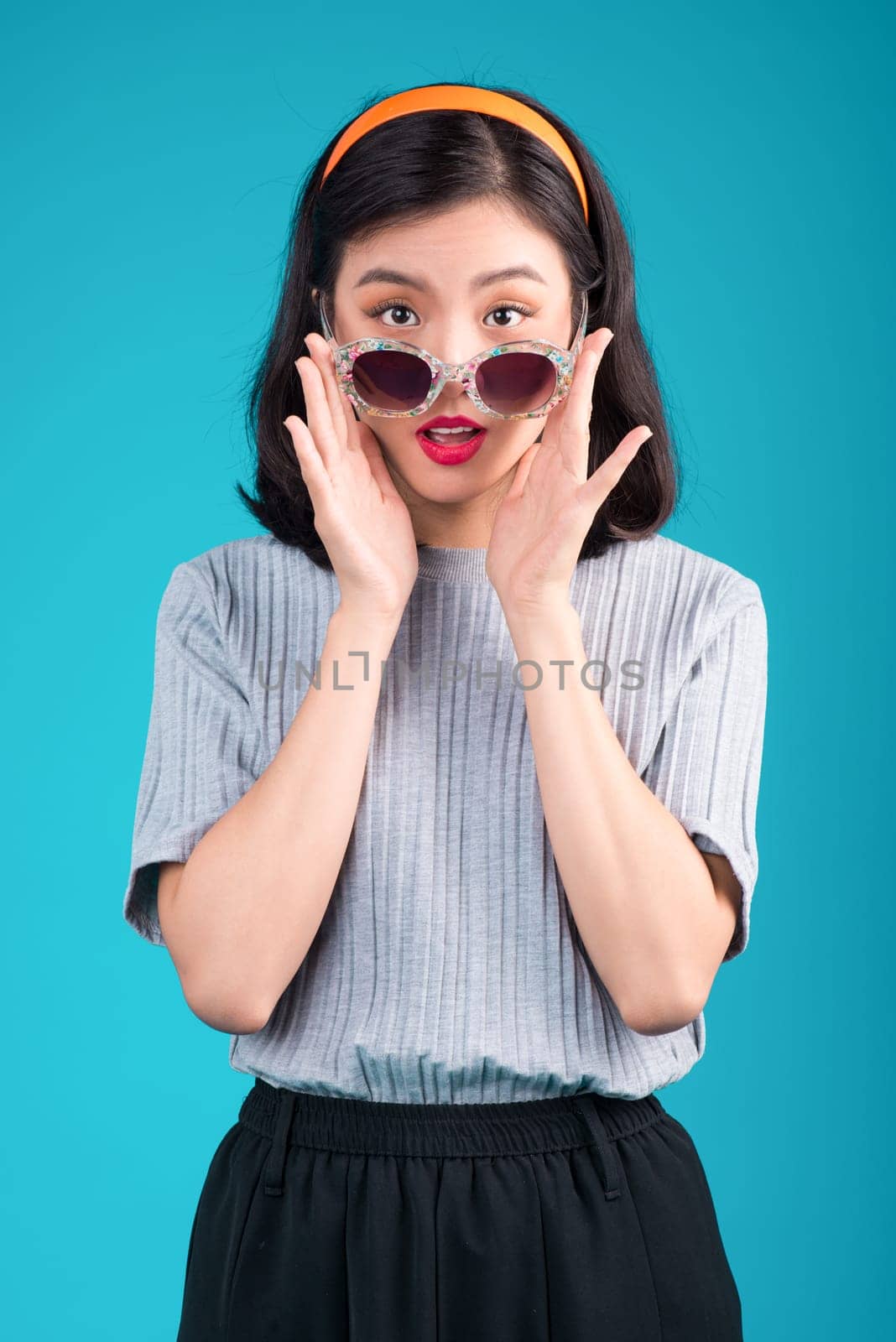 Smiling asian woman dressed in pin-up style dress wearing eyeglasses over blue.