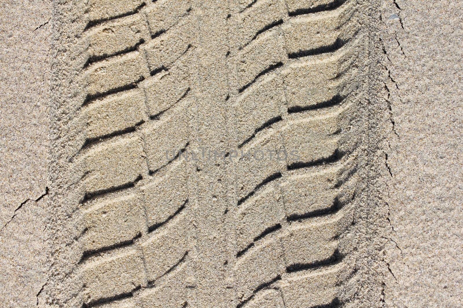 A slanted tire pattern in beige sand.