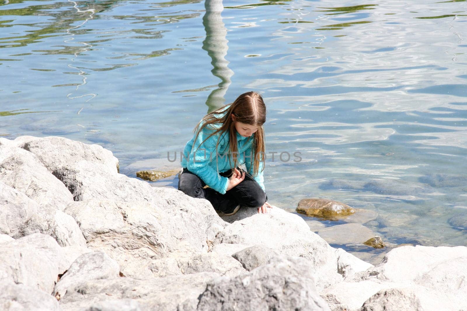 Blonde girl plays on the rocky shore of a lake.