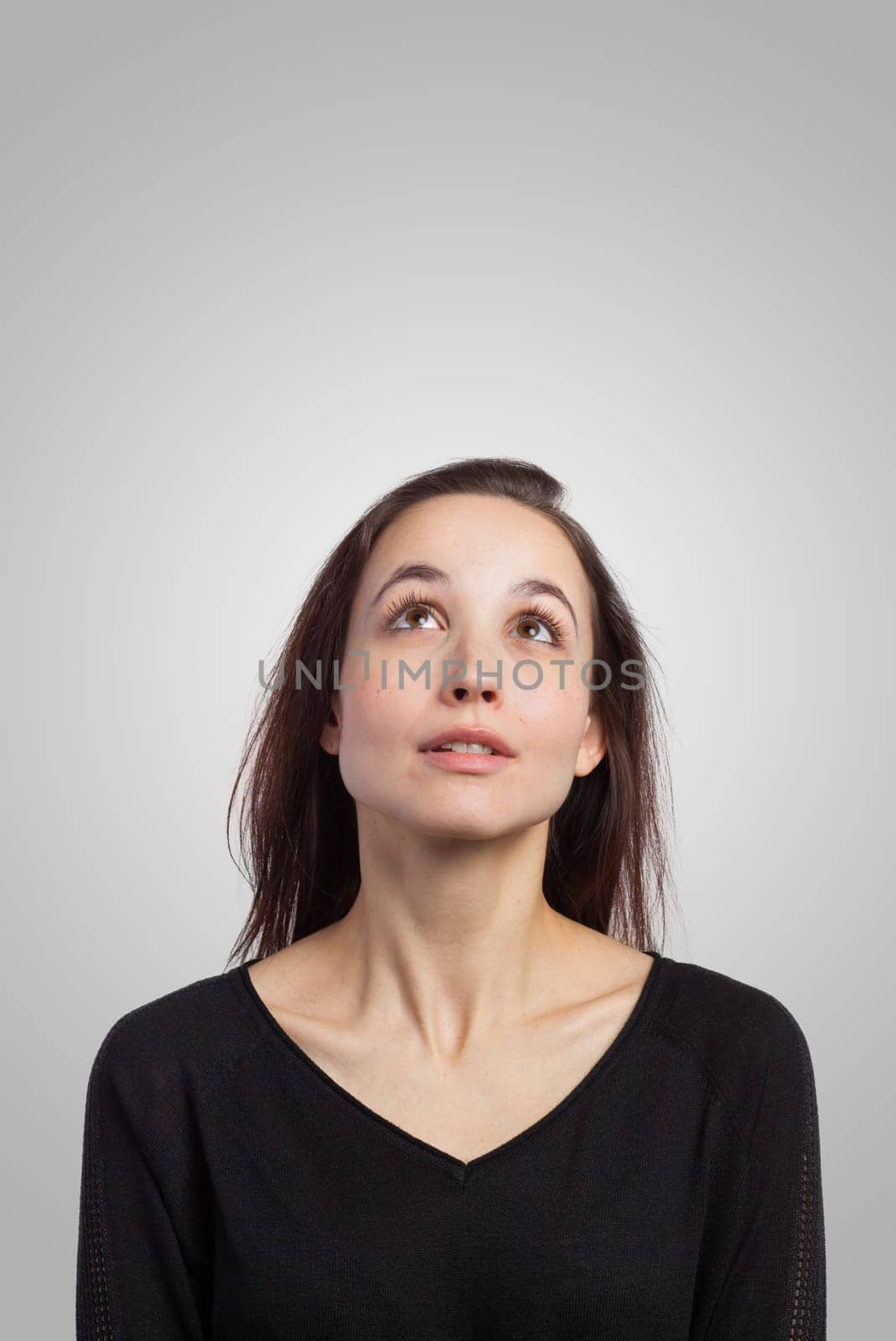 Young brunette looking up at copy space, on grey background