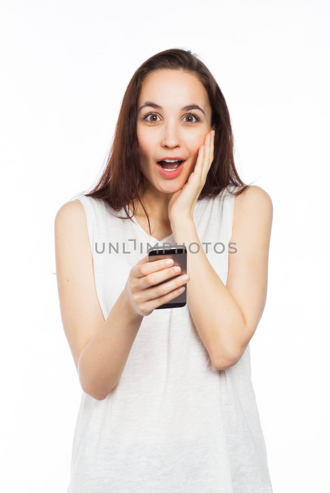 Young woman looking surprised using her phone, looking at the camera, isolated on white